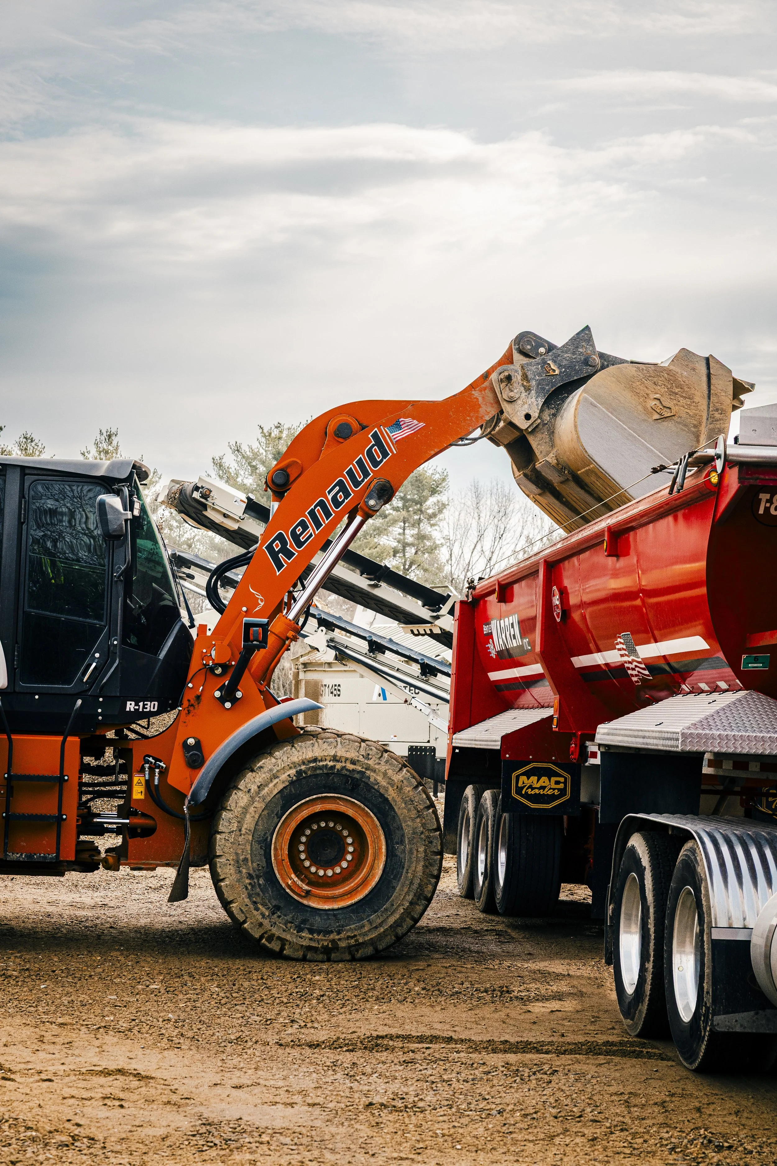 A construction vehicle with an orange arm labeled 'Reno' lifting a large metal container into a red truck.