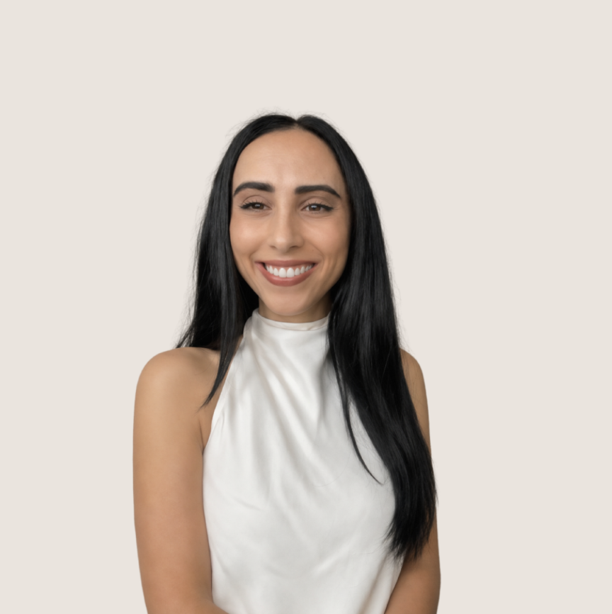 A woman with long black hair, smiling, wearing a sleeveless white top, against a plain light background.