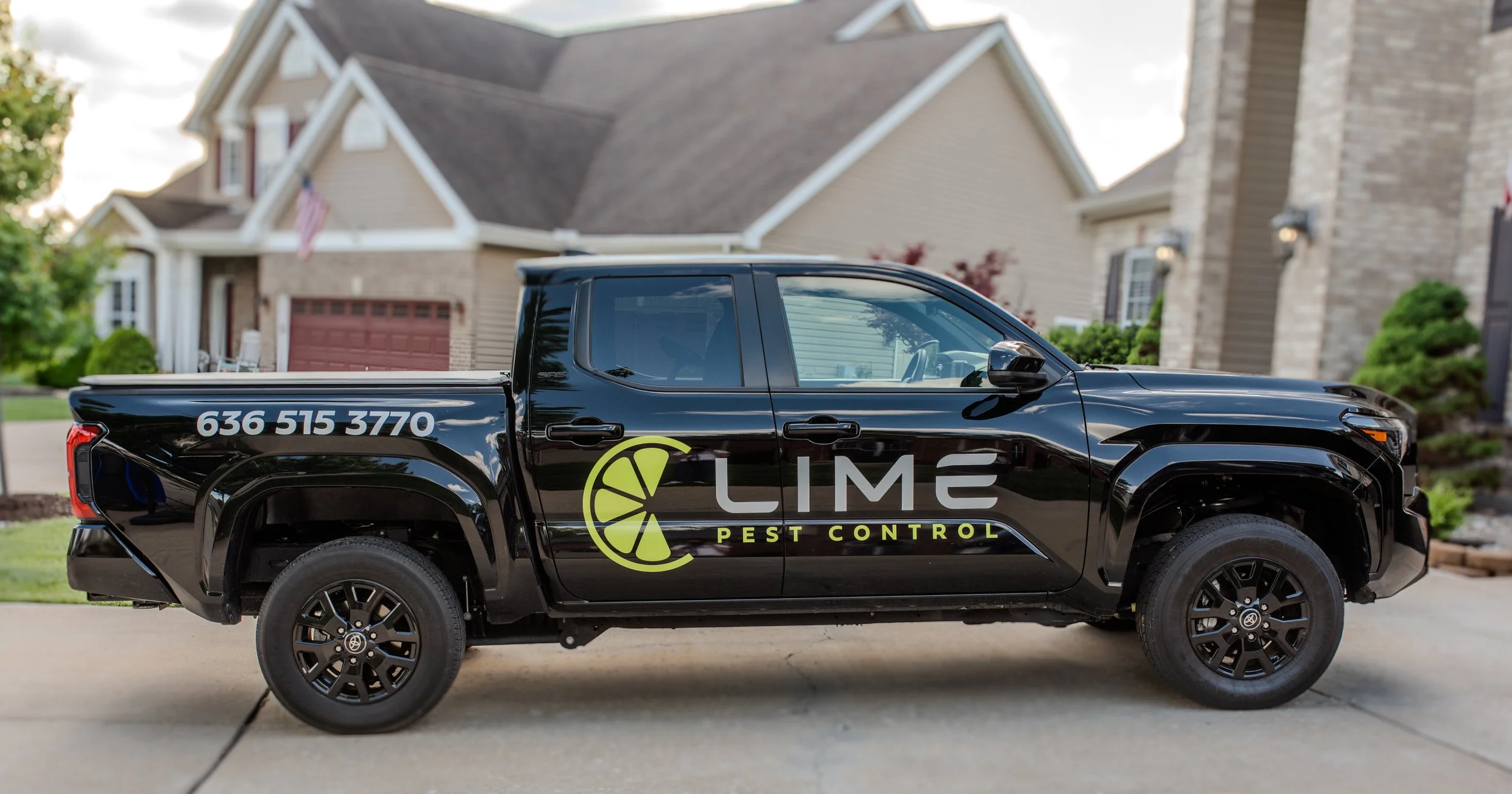 Black truck with Lime Pest Control logo and phone number parked in front of a house with beige siding and brick accents.