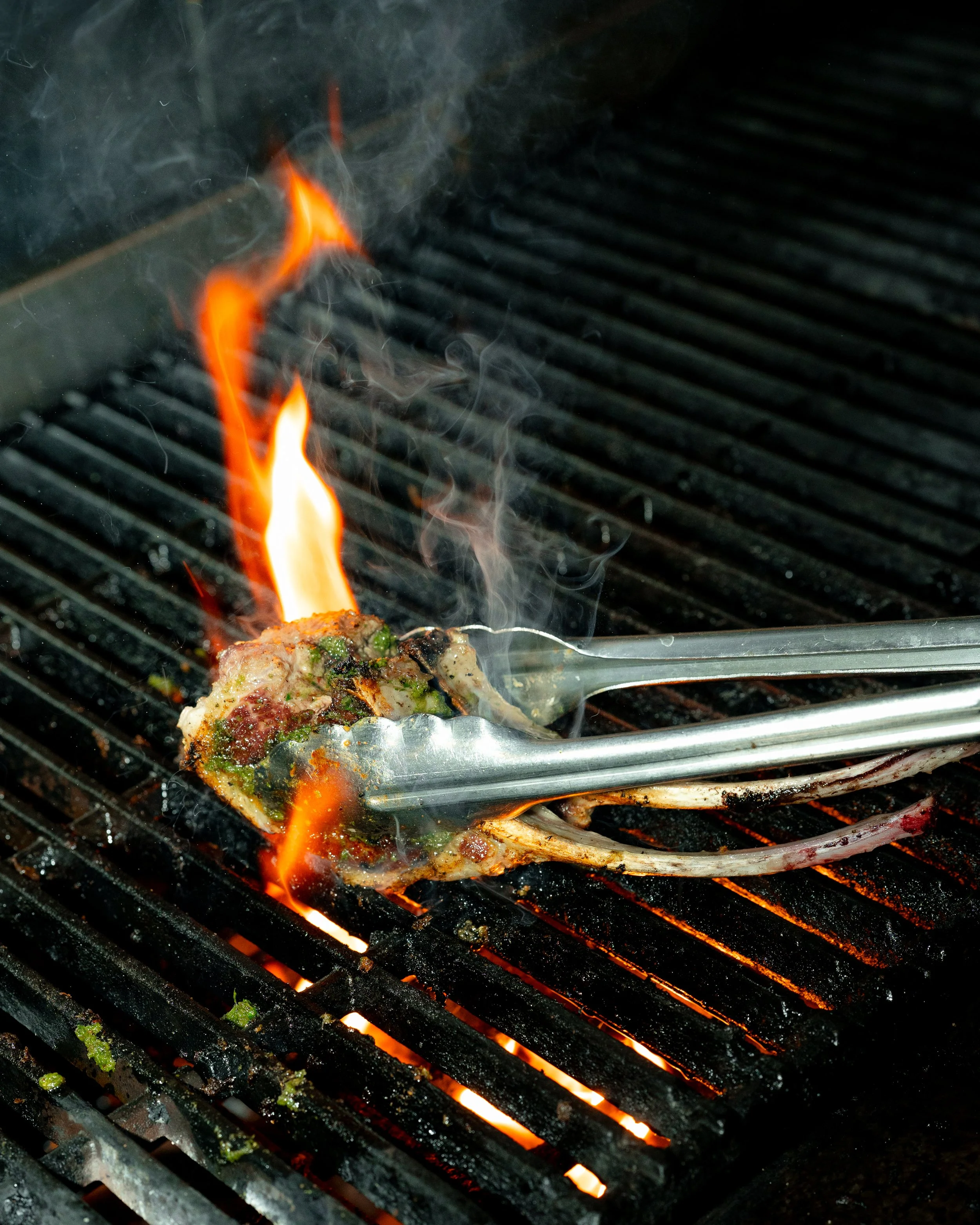 Close-up of a grill with flames and meat, with black grill grates and glowing orange flames.
