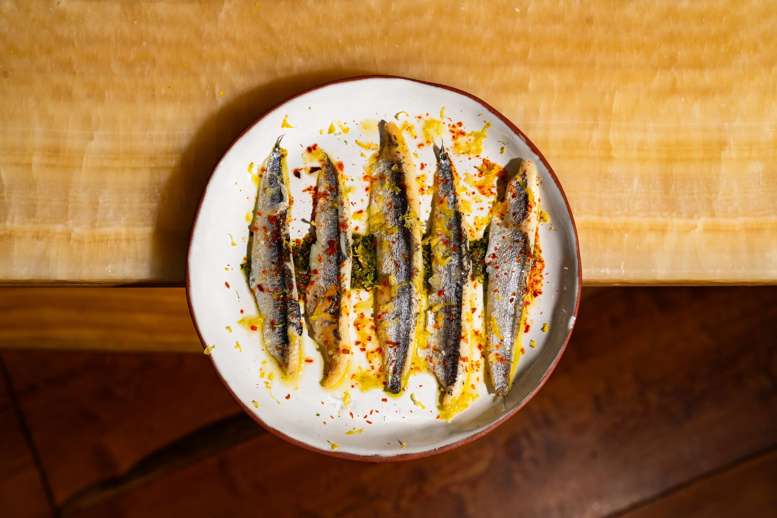 Plate of grilled fish garnished with lemon, red chili flakes, and herbs on a wooden table.