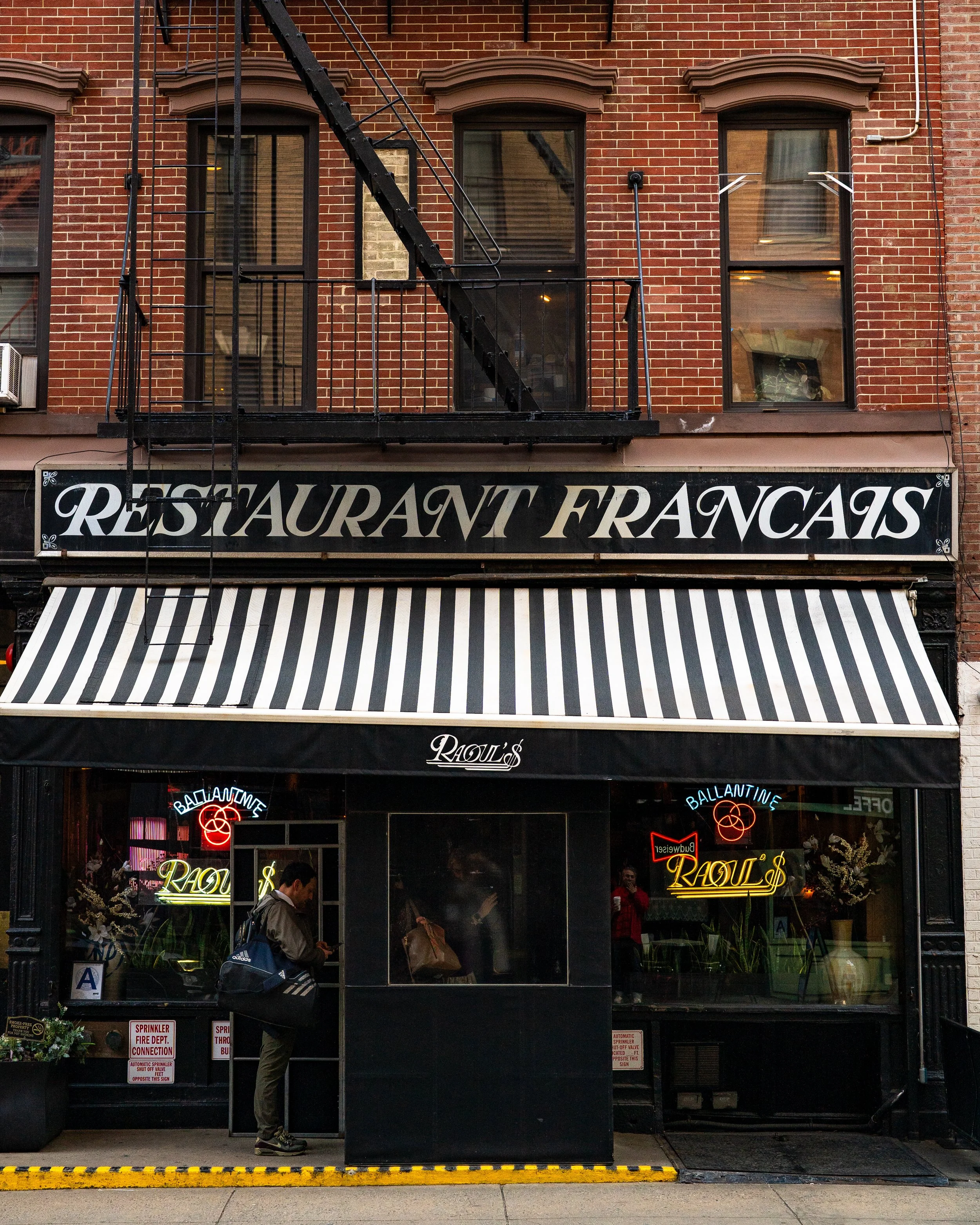The exterior of a restaurant named Régal's with a black and white striped awning, neon signs, and a brick building. People are inside and outside the restaurant.