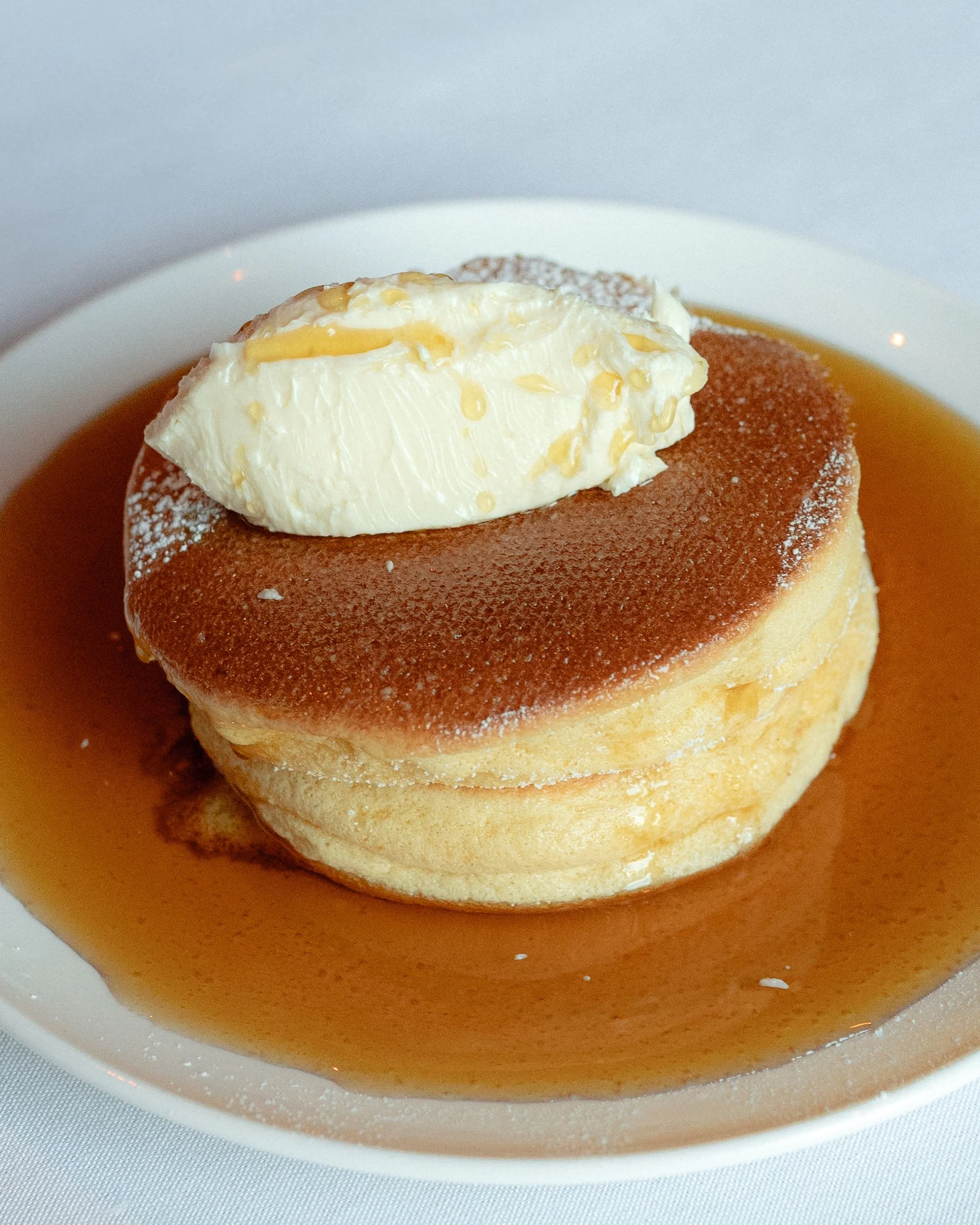 Close-up of a homemade dessert featuring a fluffy cupcake topped with a dollop of vanilla ice cream or whipped cream and sprinkled with yellow colored toppings, served on a white plate with caramel sauce.