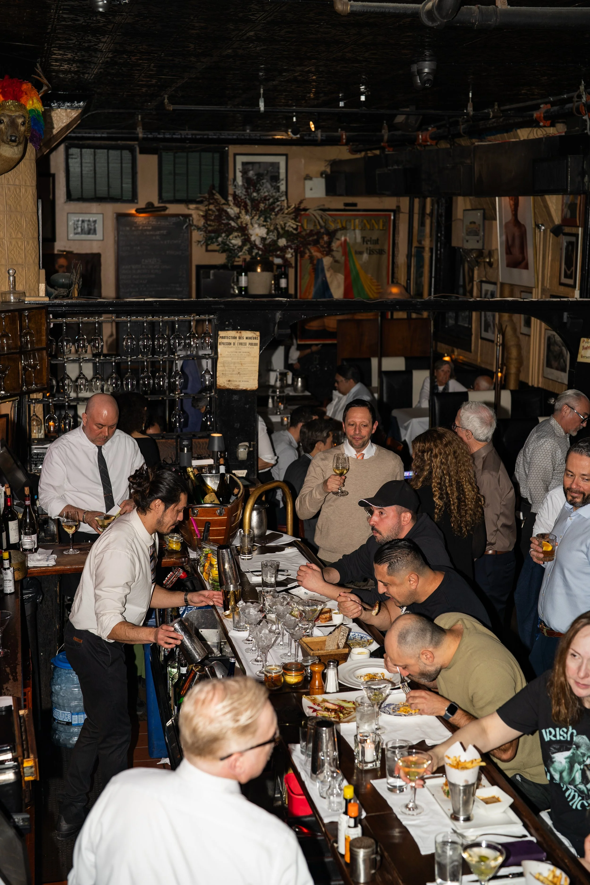 A busy restaurant with patrons dining and drinks being served. The scene includes a bar area where bartenders prepare drinks, and people are enjoying their meals and conversations.