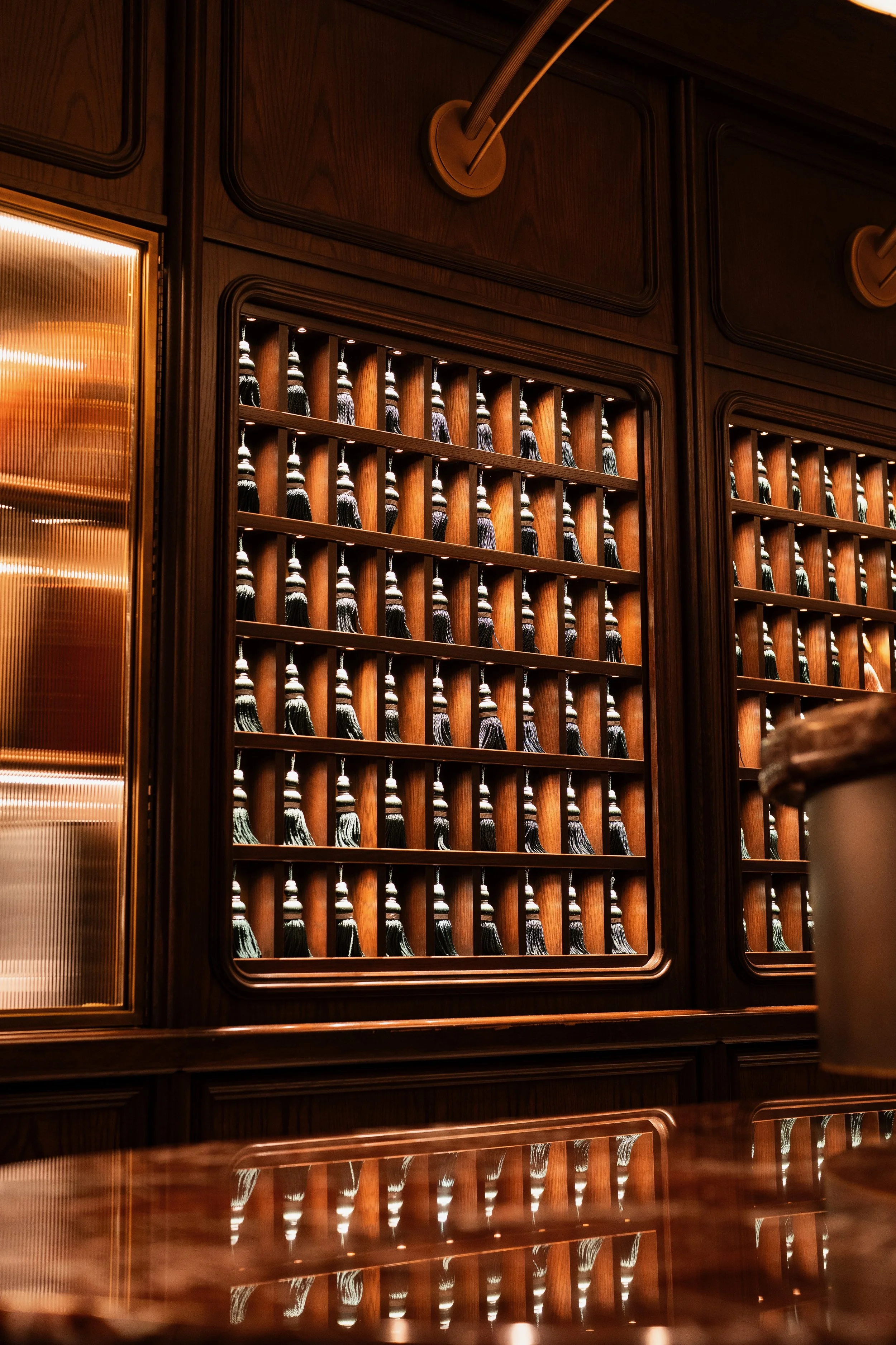 A wooden bar cabinet with numerous small bottles on wooden shelves, illuminated by small spotlights, in a warm lighting setting.