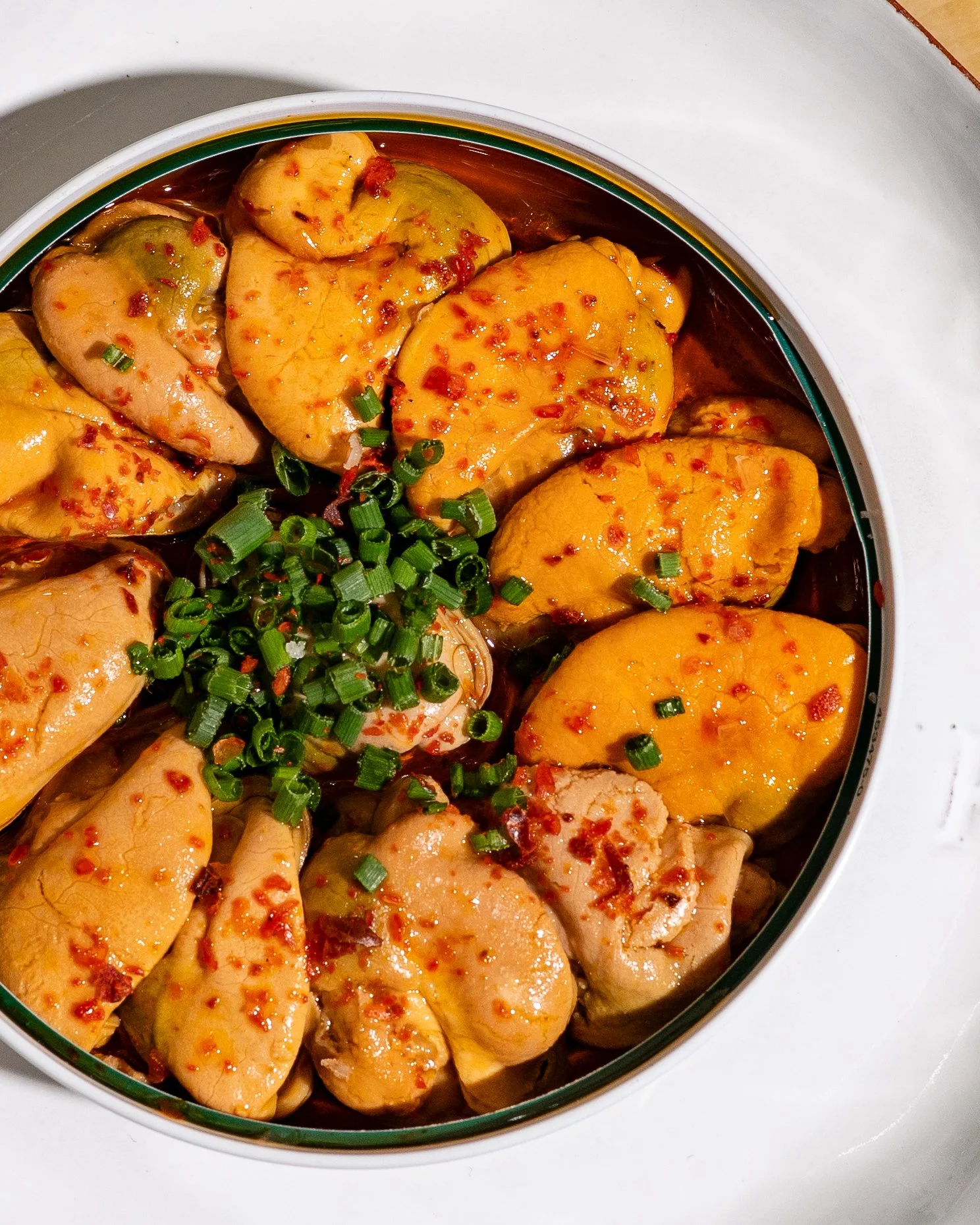 Close-up of cooked chicken pieces topped with chopped green onions and red pepper flakes in a dish.