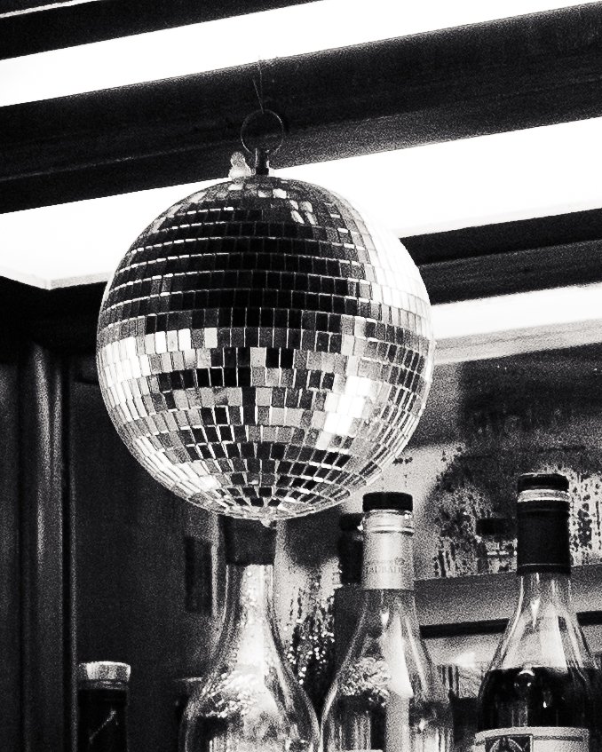A disco ball hanging from a ceiling with bottles visible below.