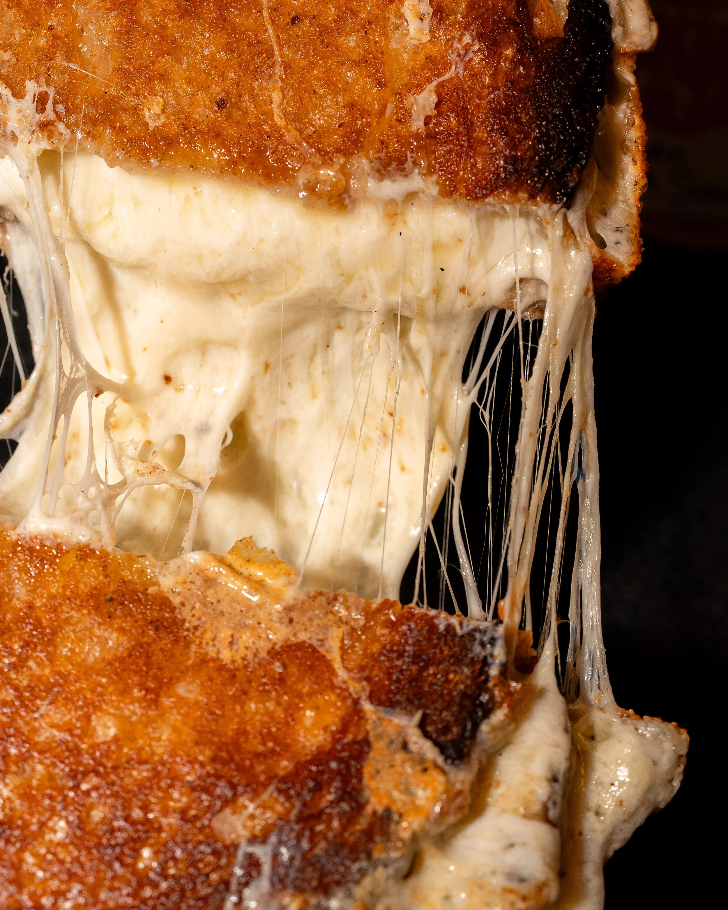 Close-up of a cheesy, crispy fried chicken with melted cheese stretching as it is pulled apart.