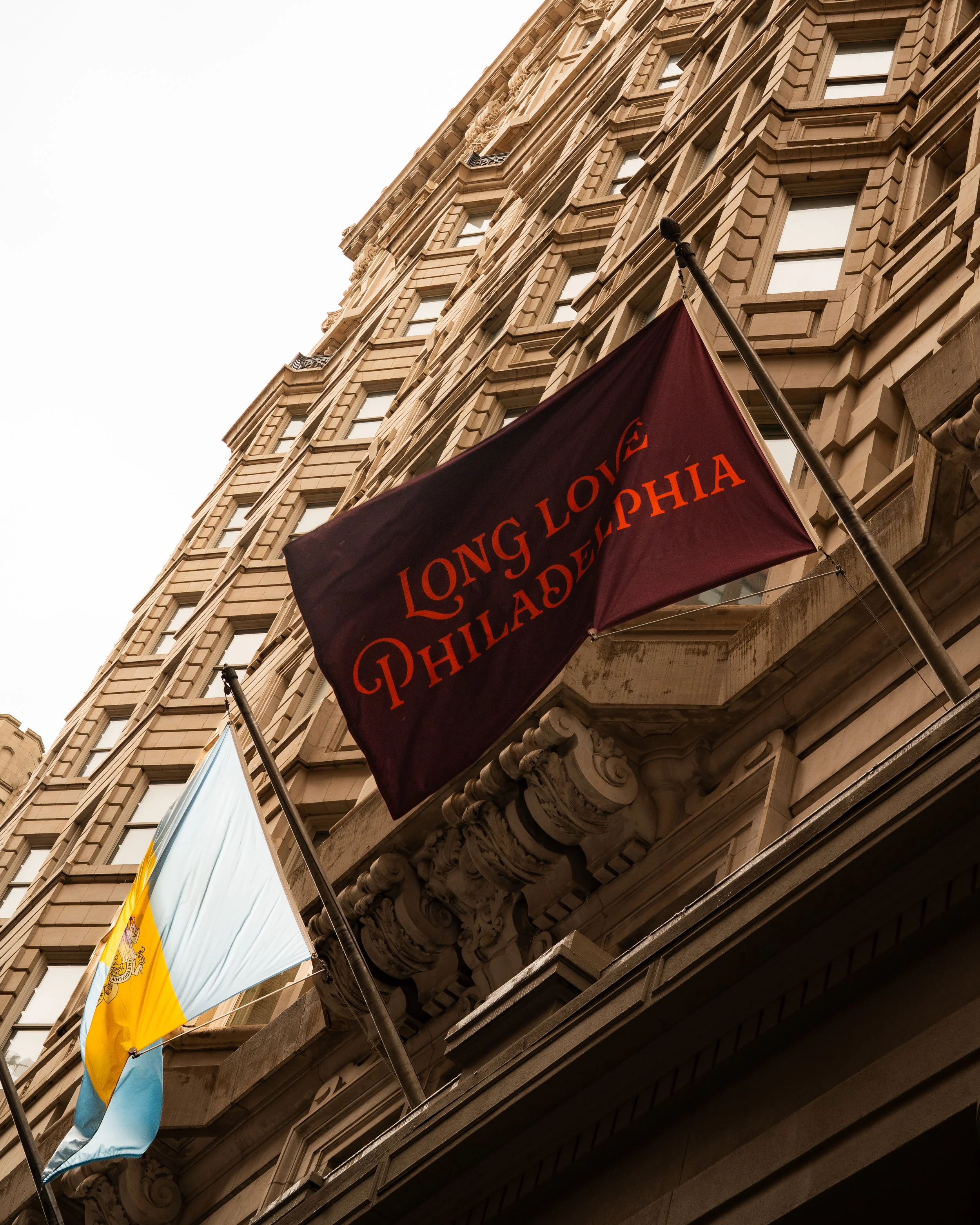 View of historical building with ornate stone facade, featuring multiple windows and decorative details, with flags hanging below.