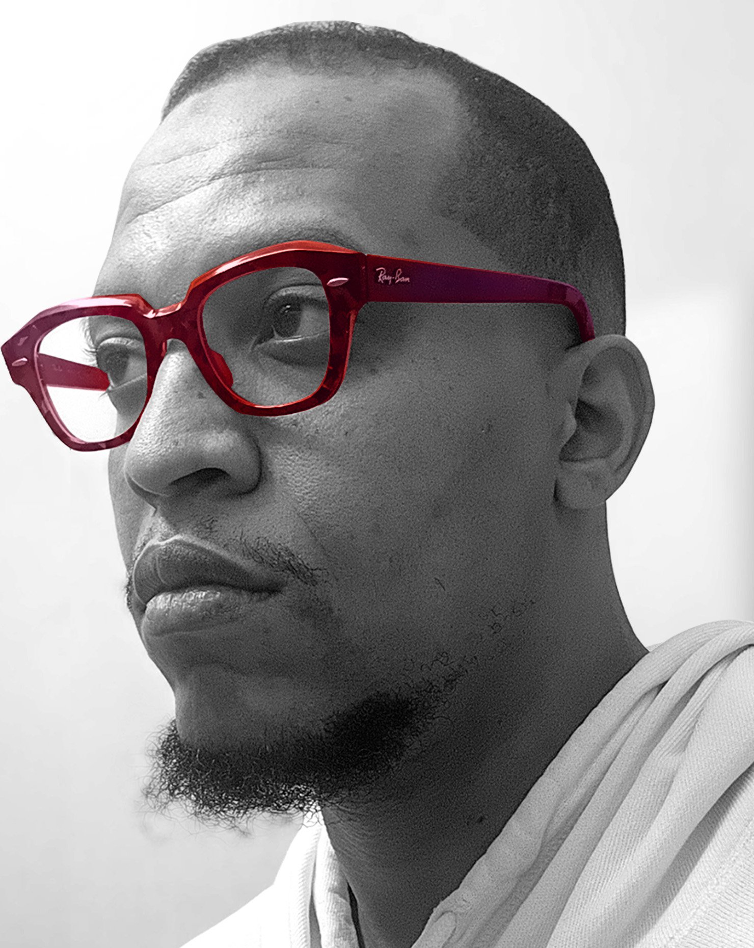 Black and white photograph of a man facing left, wearing Ray Ban glasses that are colored red.