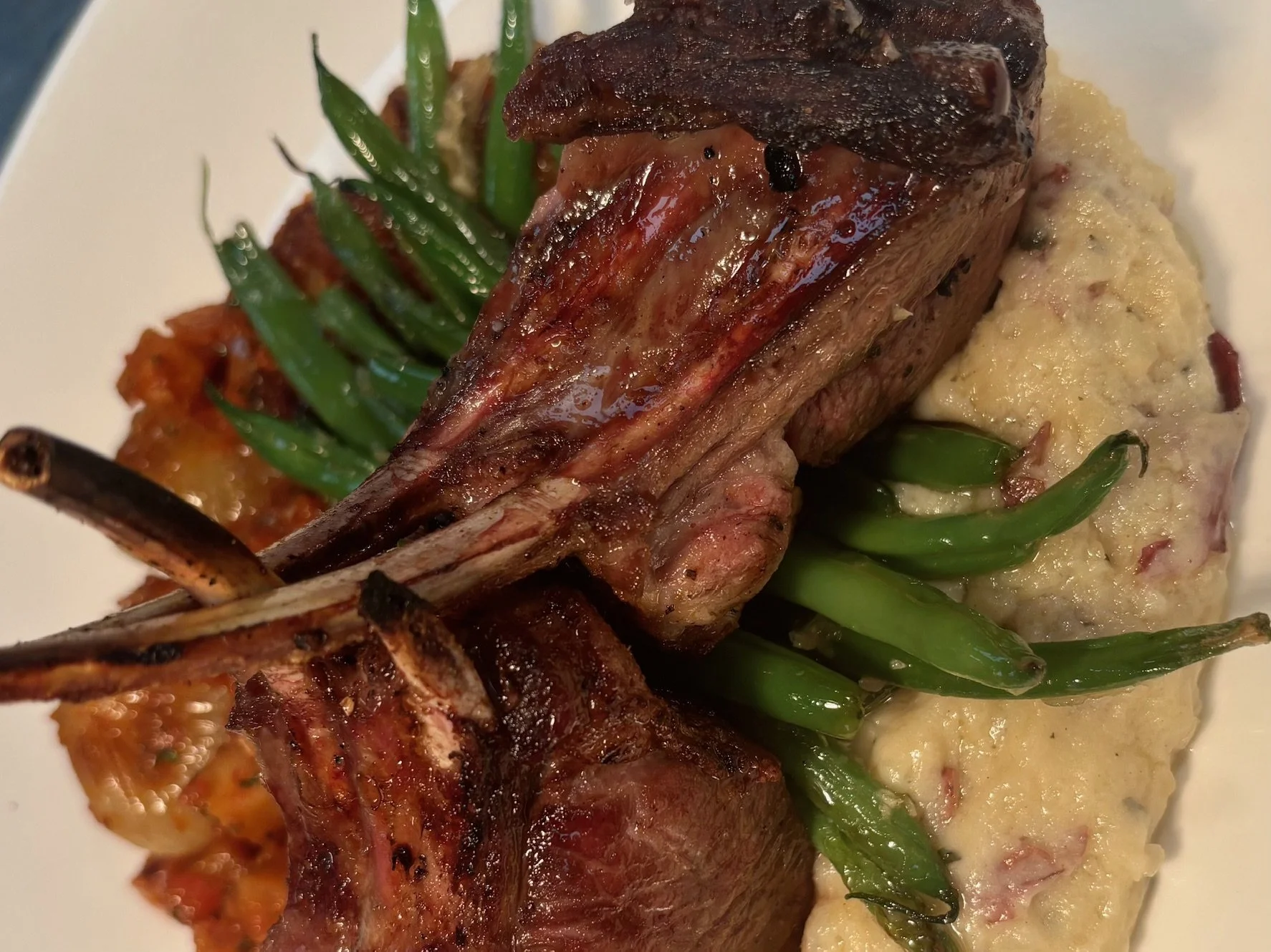 Close-up of a plated meal featuring grilled ribs, green beans, and a serving of mashed potatoes with bacon bits.