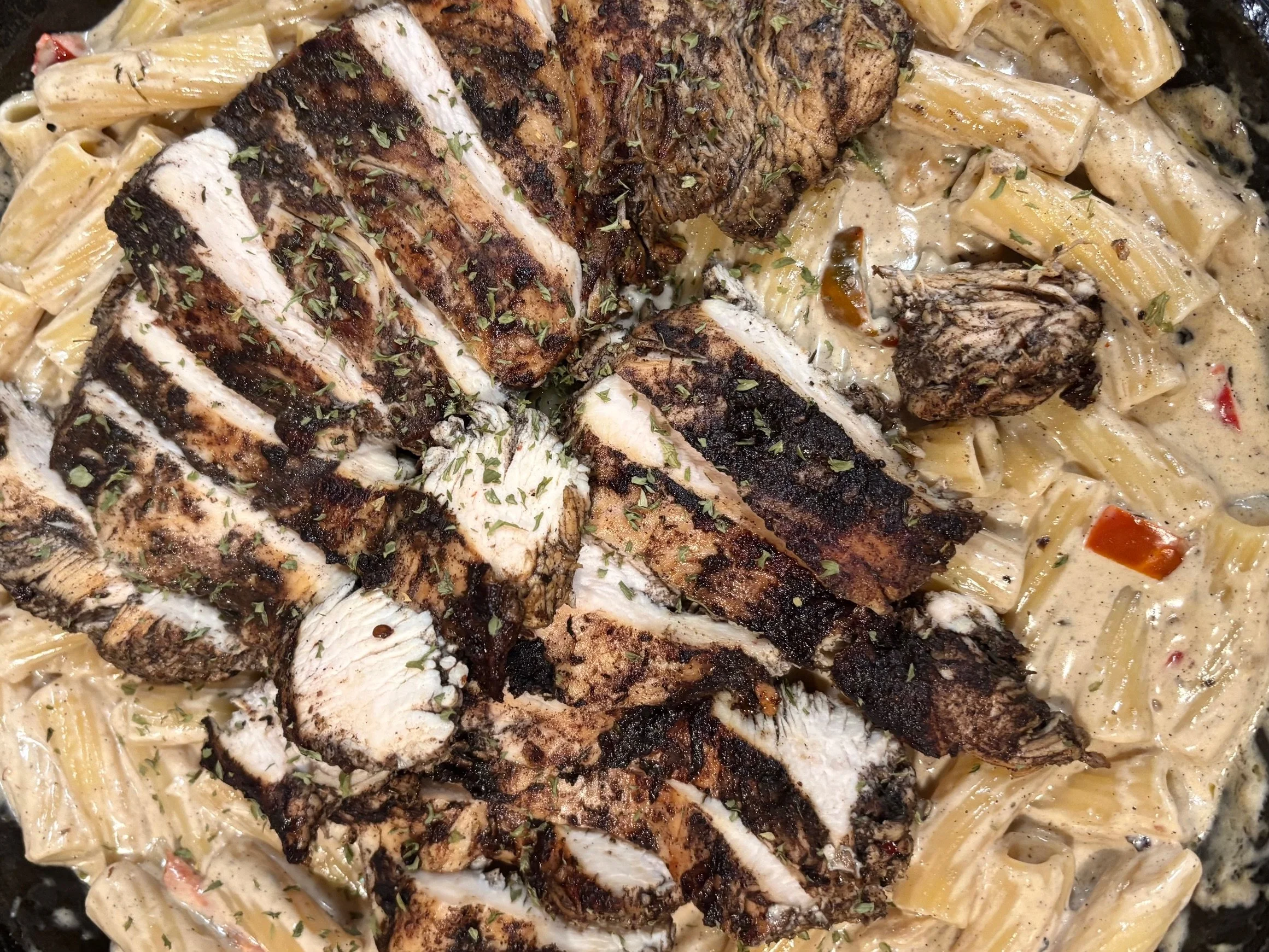 Close-up of grilled pork chops resting on a bed of creamy pasta with vegetables, garnished with chopped herbs.