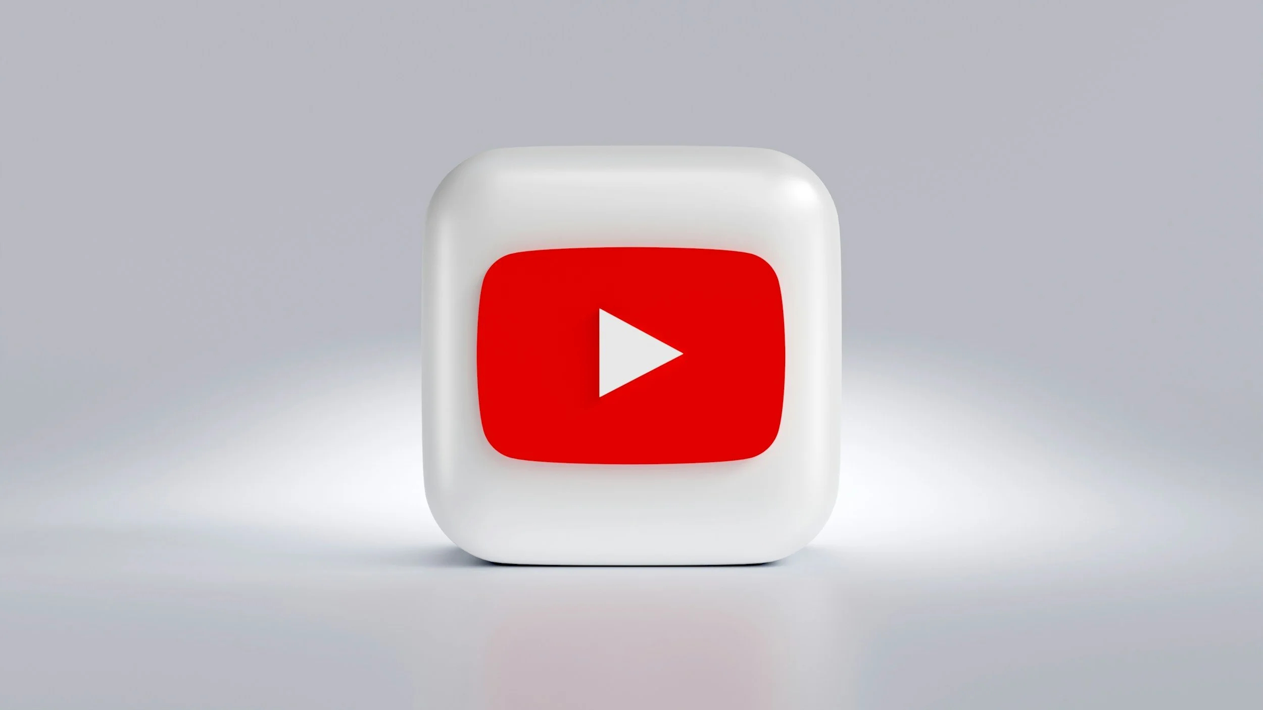 A white cube with a red YouTube play button icon on its front side, placed against a gray background.