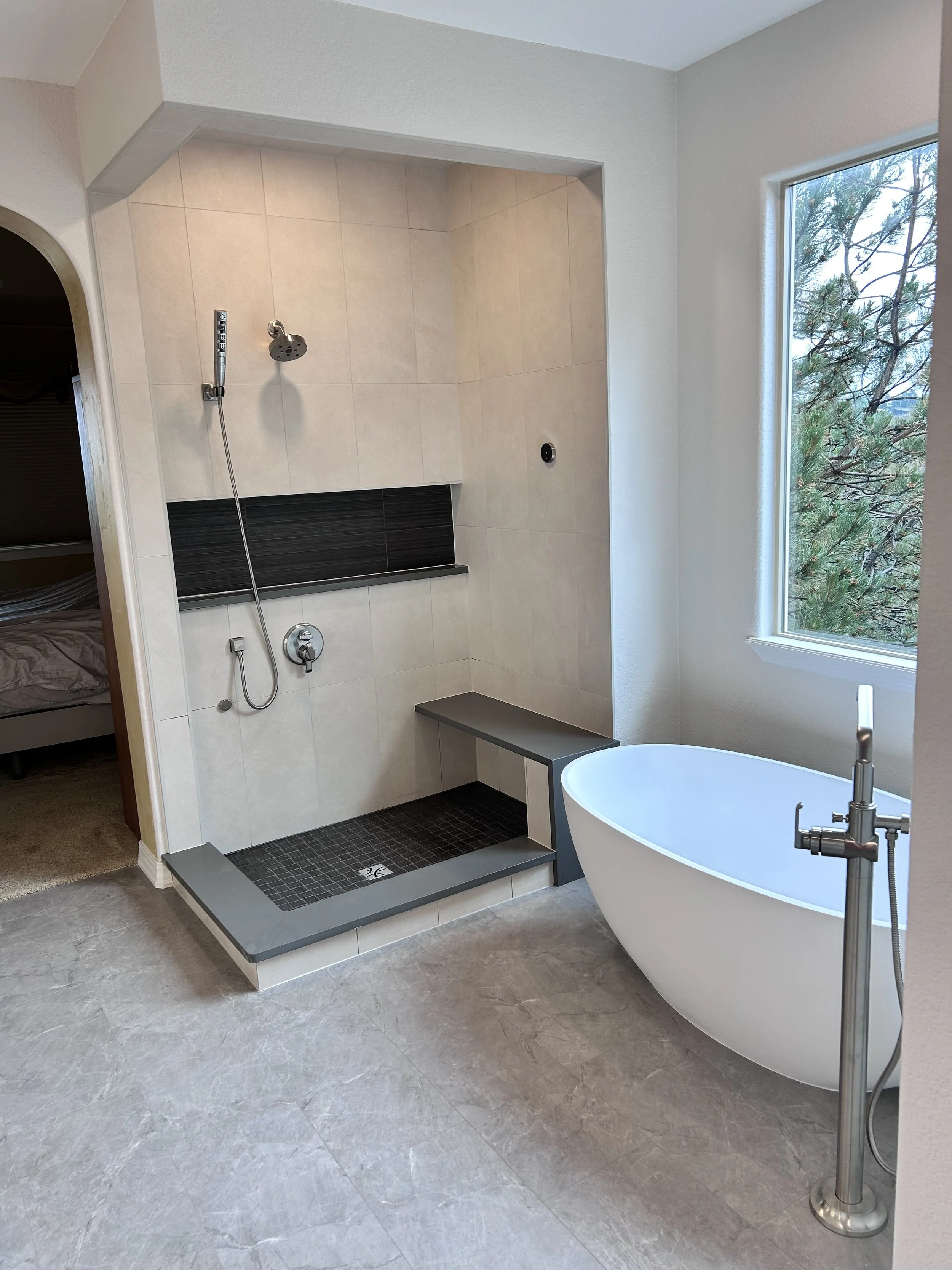 Modern bathroom with walk-in shower, freestanding bathtub, large window, and gray marble floor.