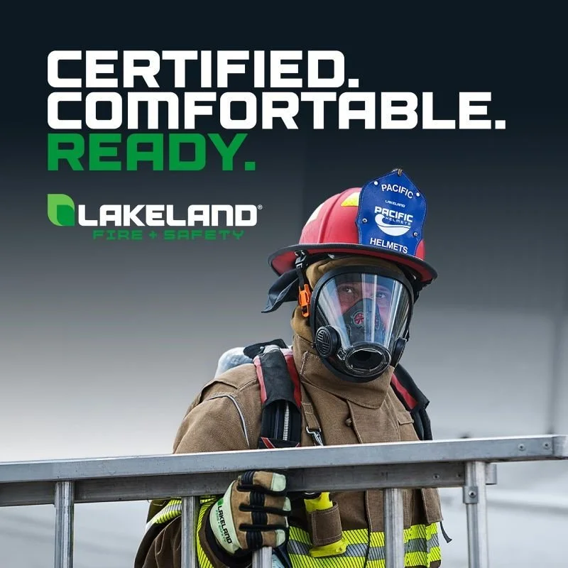 Un bombero con equipo de protección, máscara facial y casco rojo, de pie detrás de una barandilla de metal, con un fondo oscuro y el texto"Certificado. Cómodo. Listo." y el logotipo de Lakeland Fire + Safety.