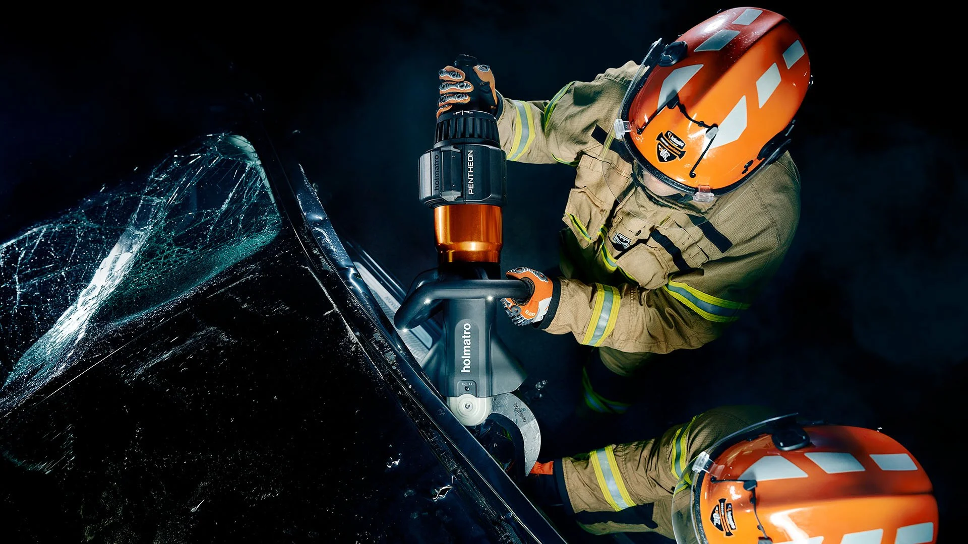 Un bombero con casco naranja y equipo protector trabaja con herramienta eléctrica en un coche con parabrisas roto.