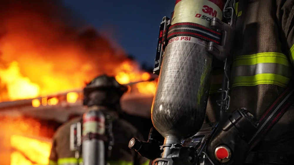 Bomberos luchando contra un incendio intenso con llamas y humo en el fondo.