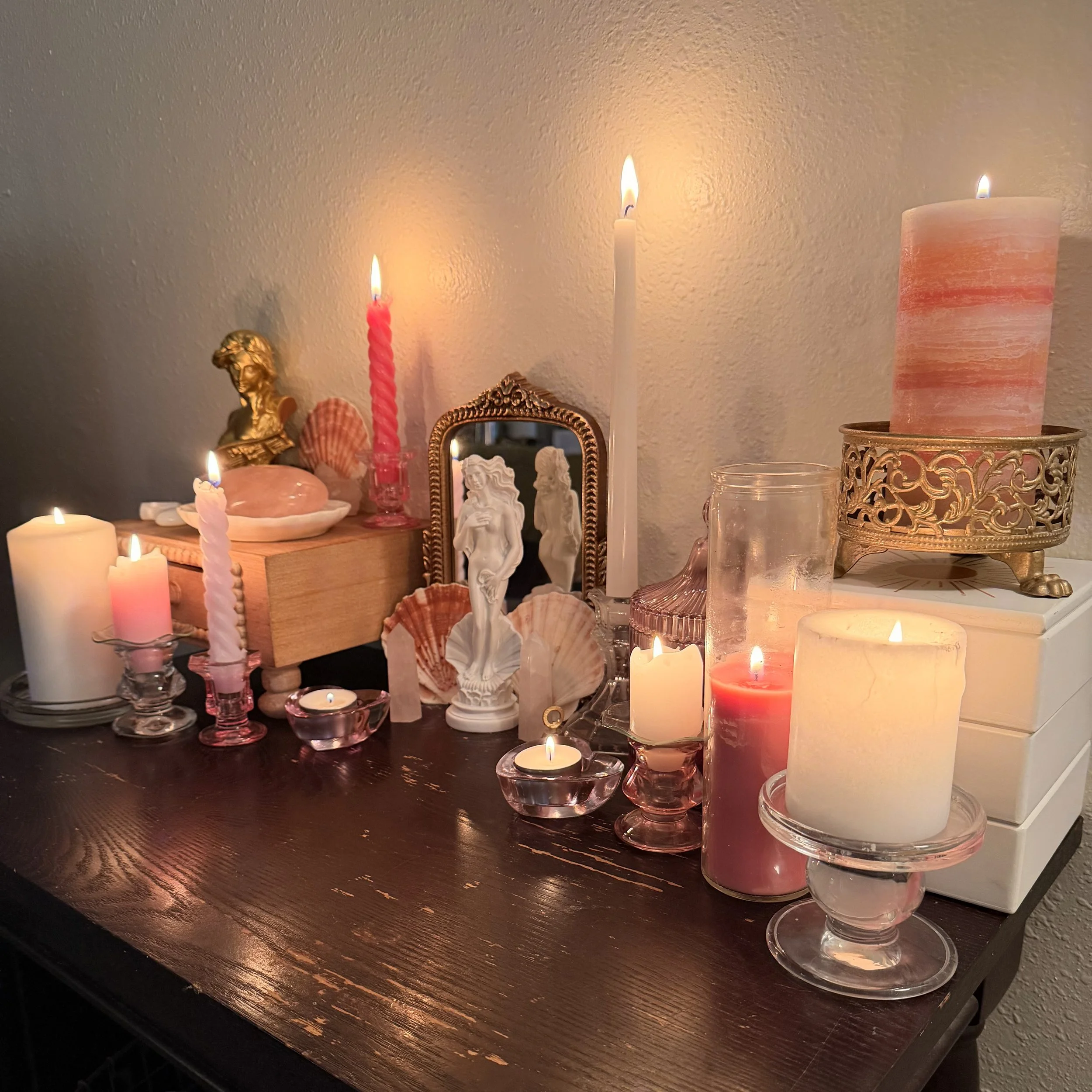 Decorative arrangement with lit candles, seashells, small sculptures, a mirror, and a jewelry box on a dark wooden surface.
