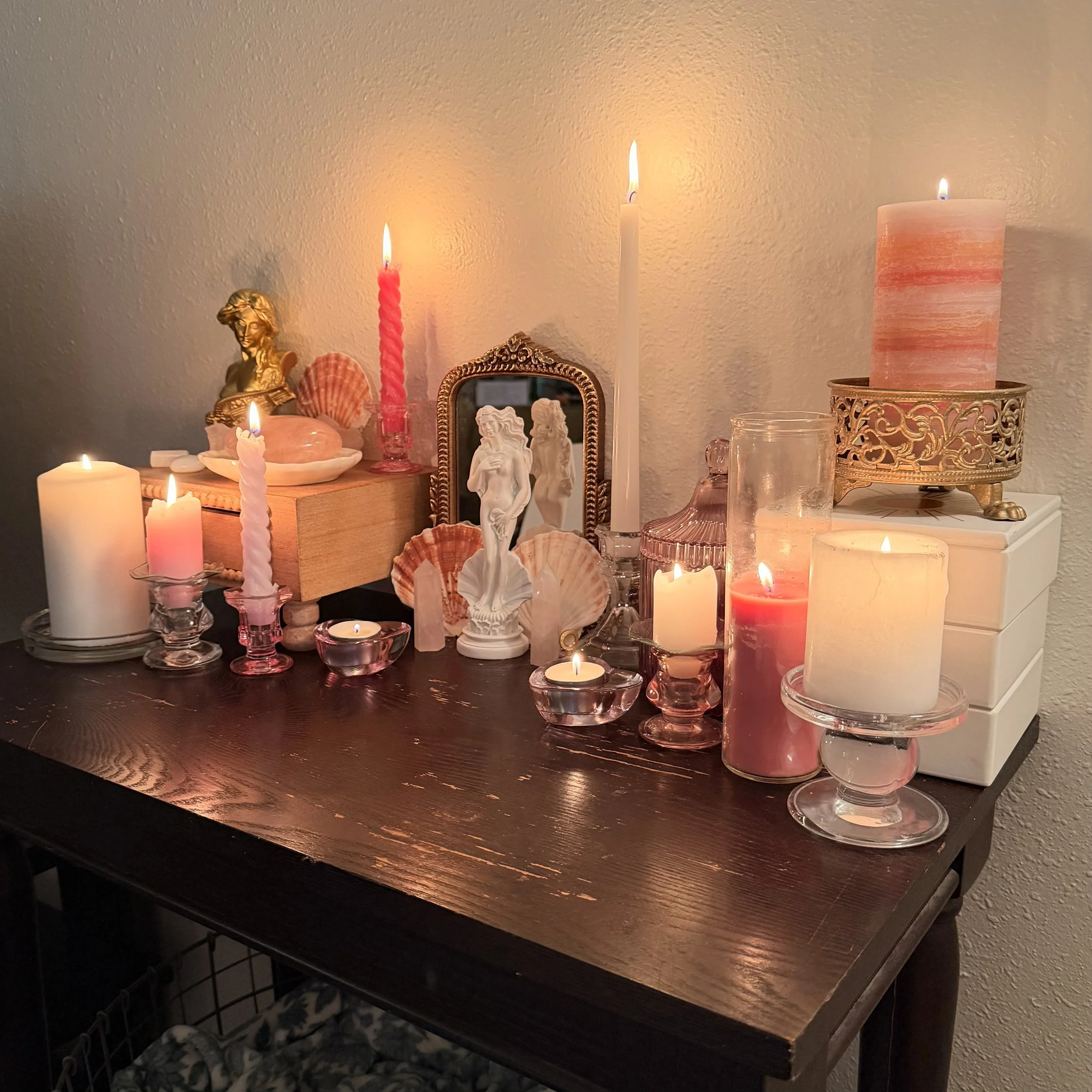 A dark wooden table with various candles, decorative figurines, shells, and a mirror against a light-colored wall.