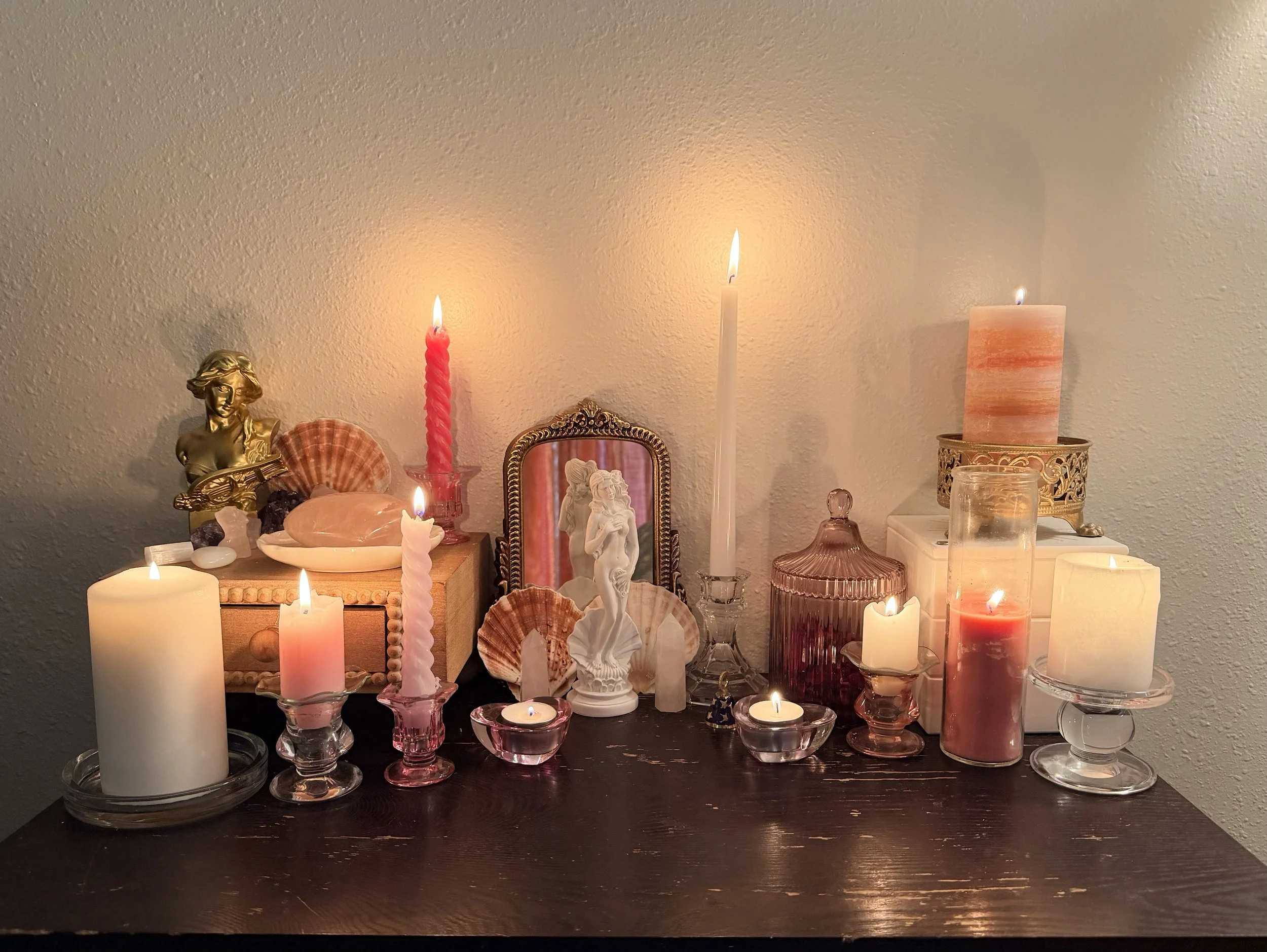 A wooden table with various candles, decorative figurines, shells, and glass containers, creating a cozy ambiance.