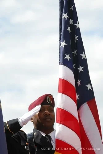 A person in military uniform salutes while holding an American flag.