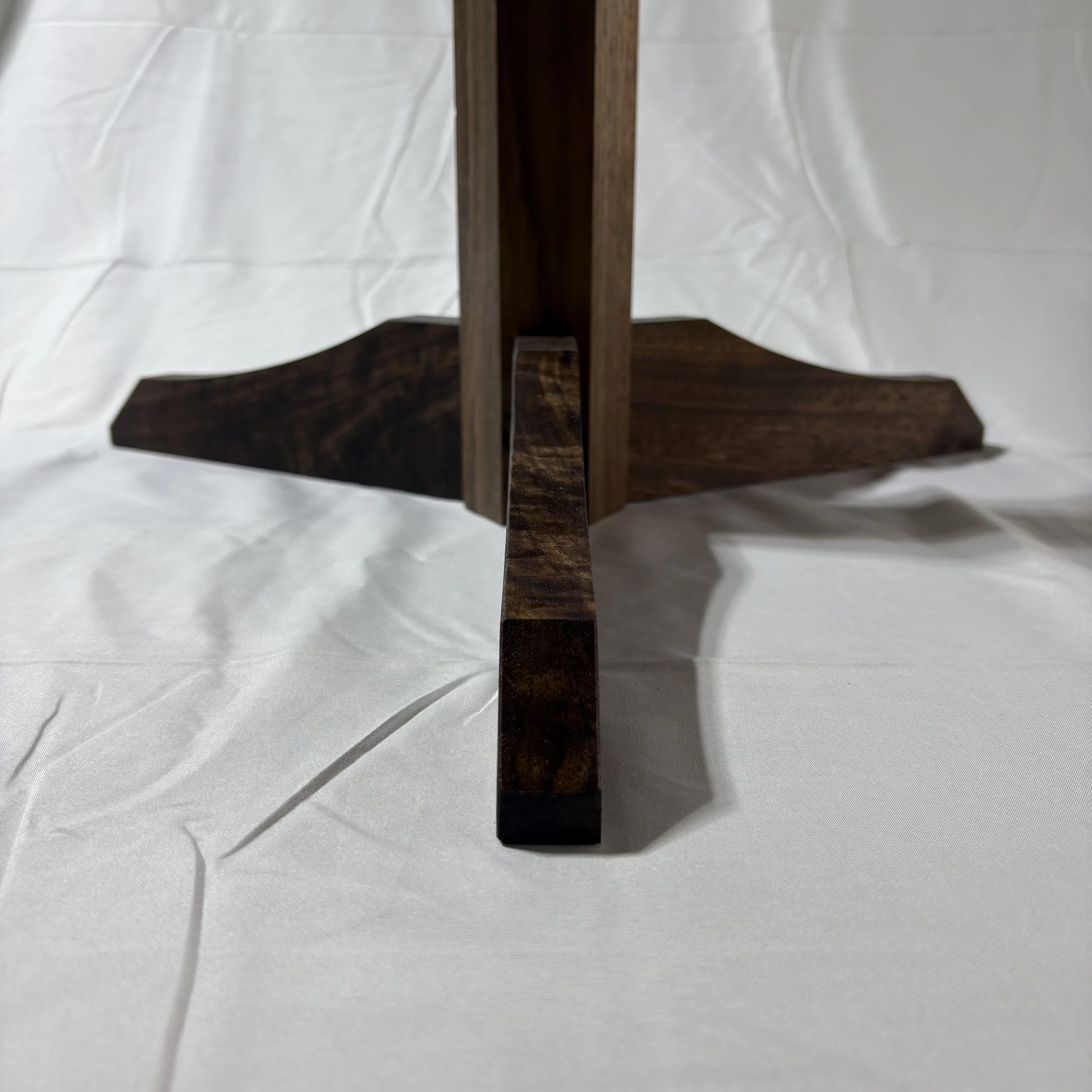 A wooden table with four legs, shown from a close-up underside view, placed on a crinkled white fabric background.