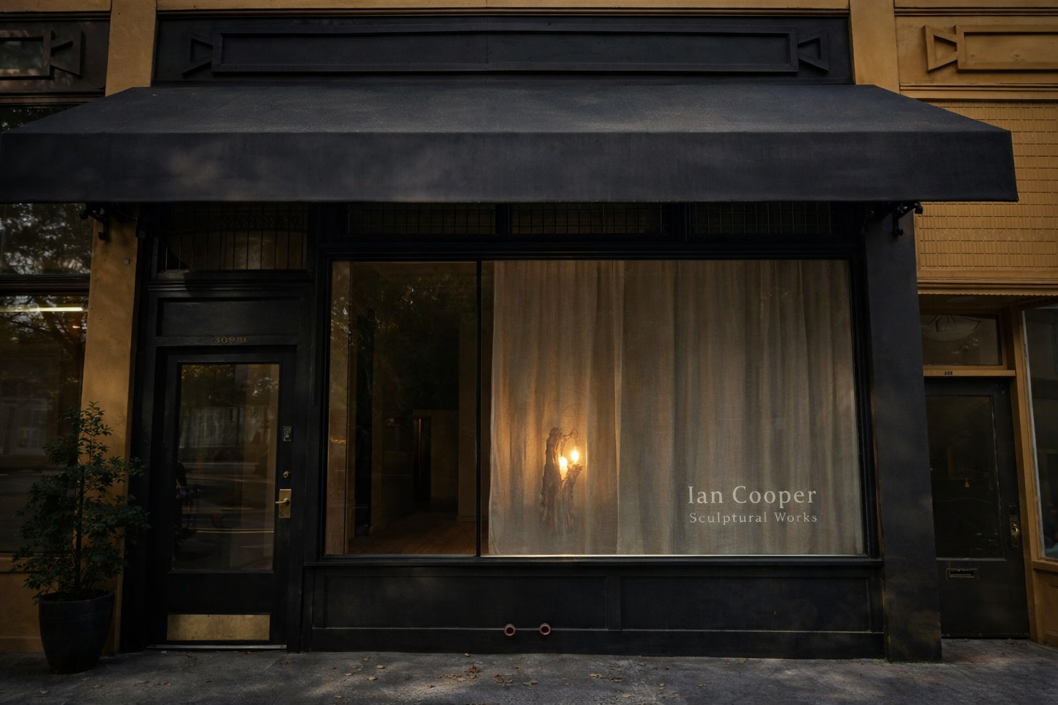 Art gallery storefront with a large window, black awning, and a door, displaying the name 'Ian Cooper Sculptural Works' with a sculpture inside visible through the window.