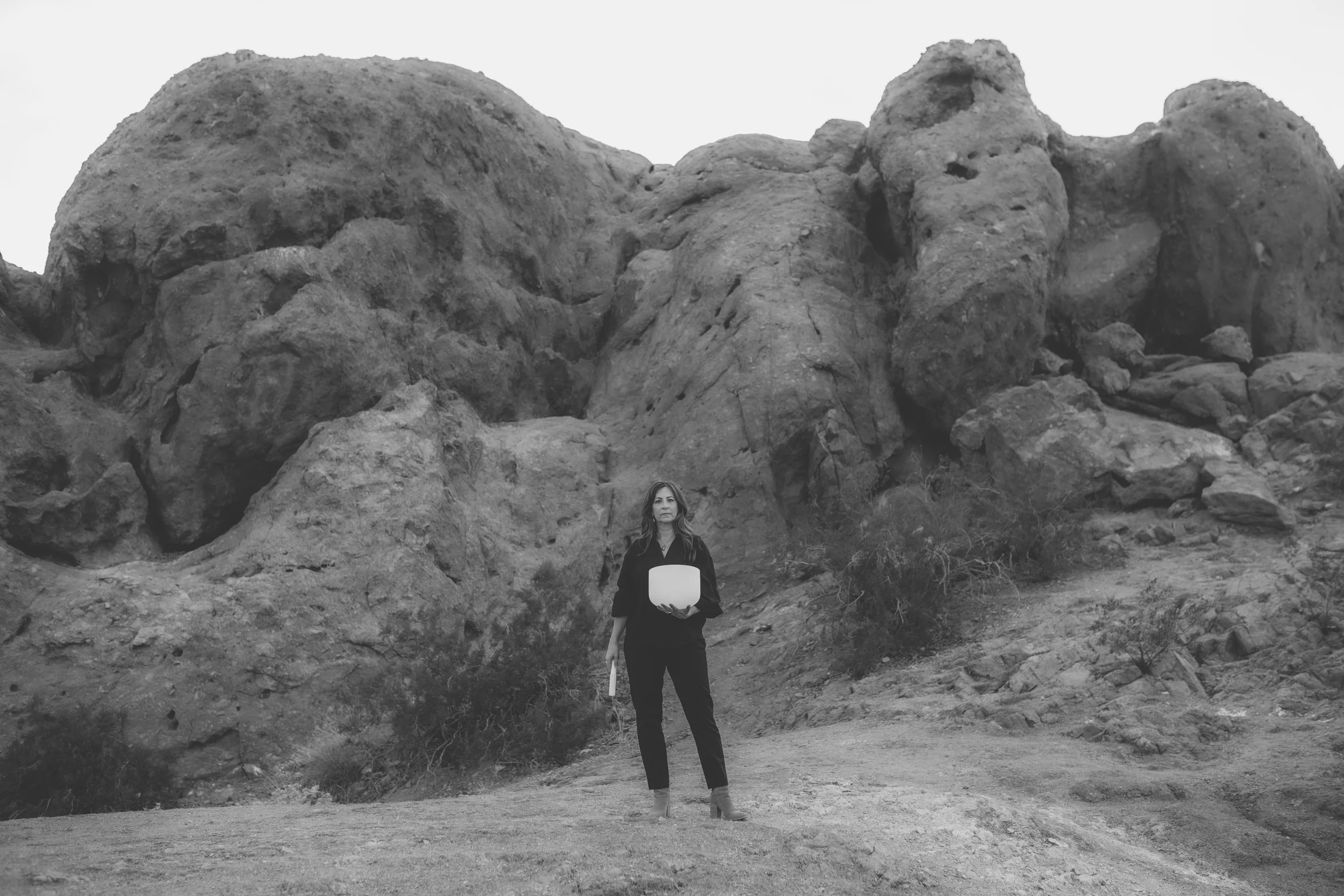 A woman standing outdoors in front of large rocky formations, holding a white bowl.