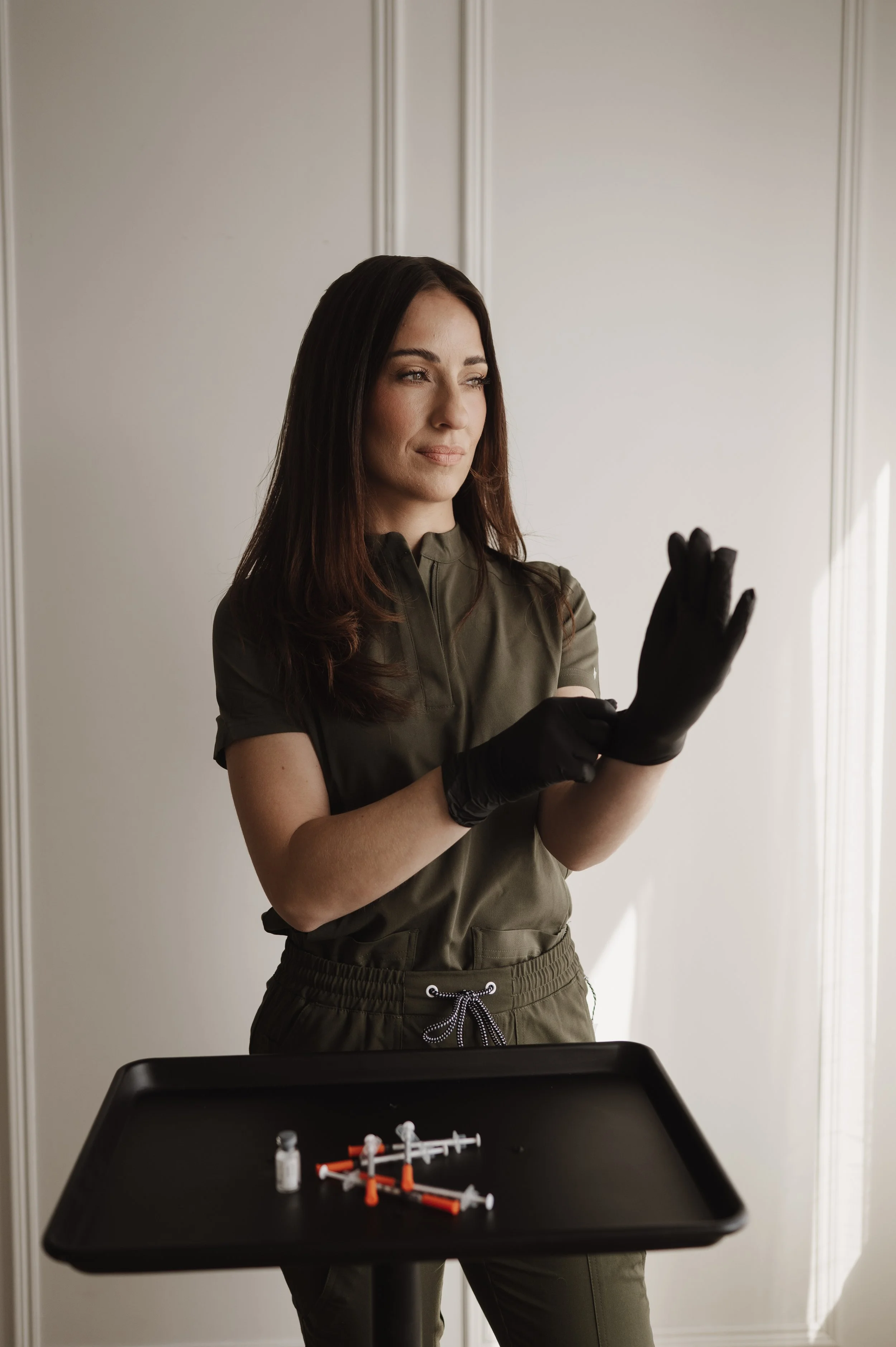 A woman in scrubs and black gloves is preparing syringes on a black tray.