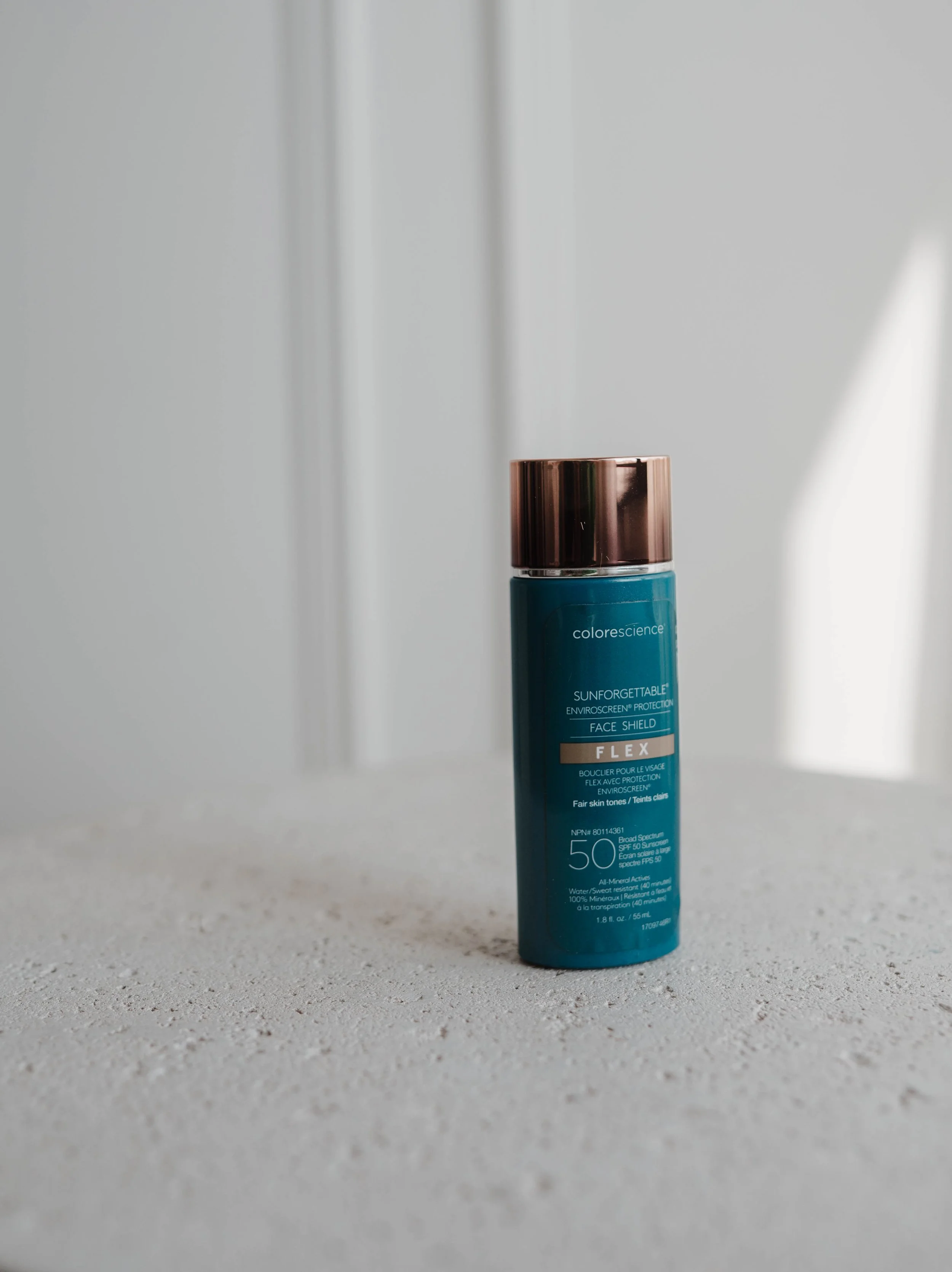A blue bottle of Colorescience Sunforgettable face shield sunscreen with a bronze cap, placed on a light-colored textured surface.