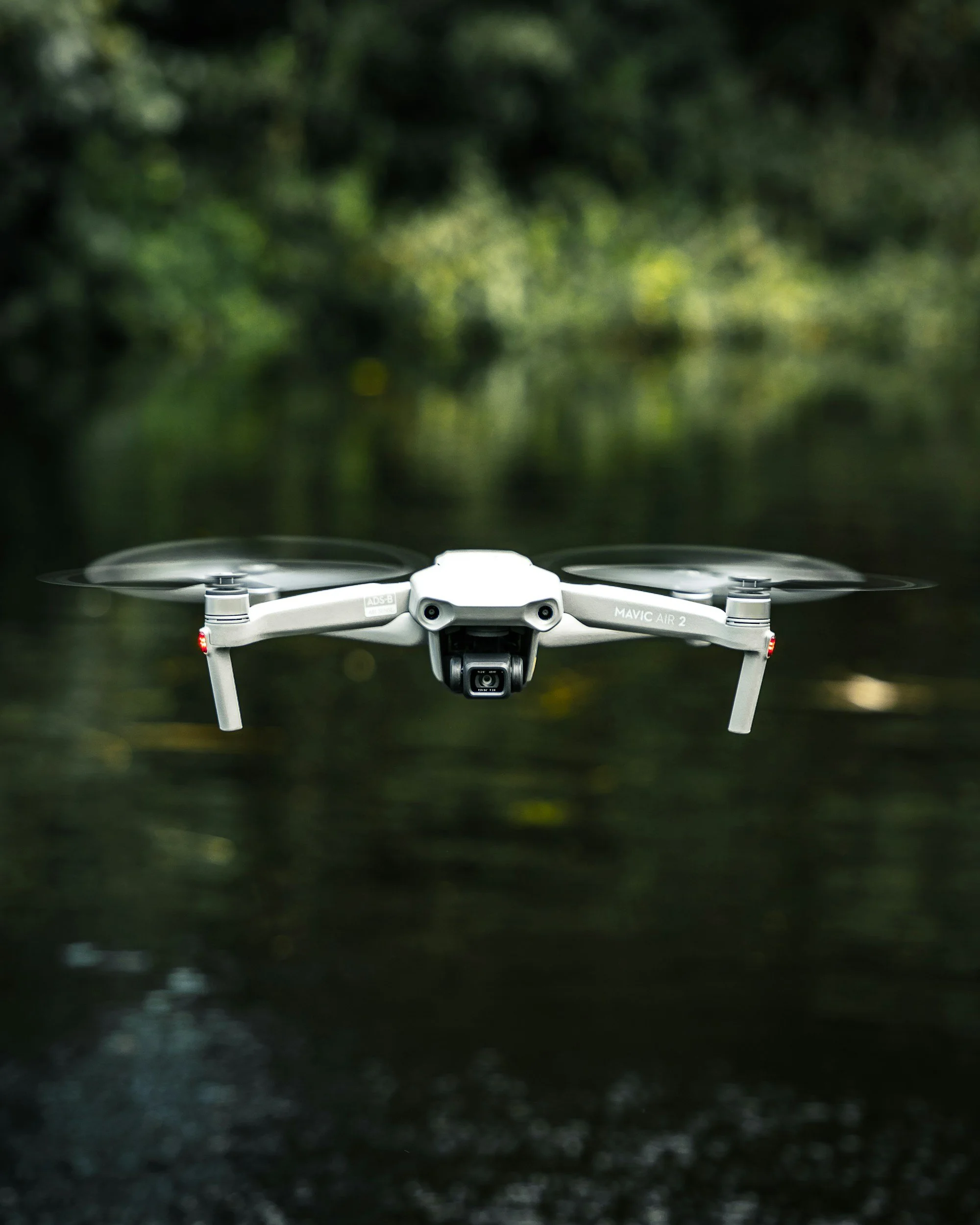 A drone flying low over a dirt path surrounded by lush green trees in a forest.