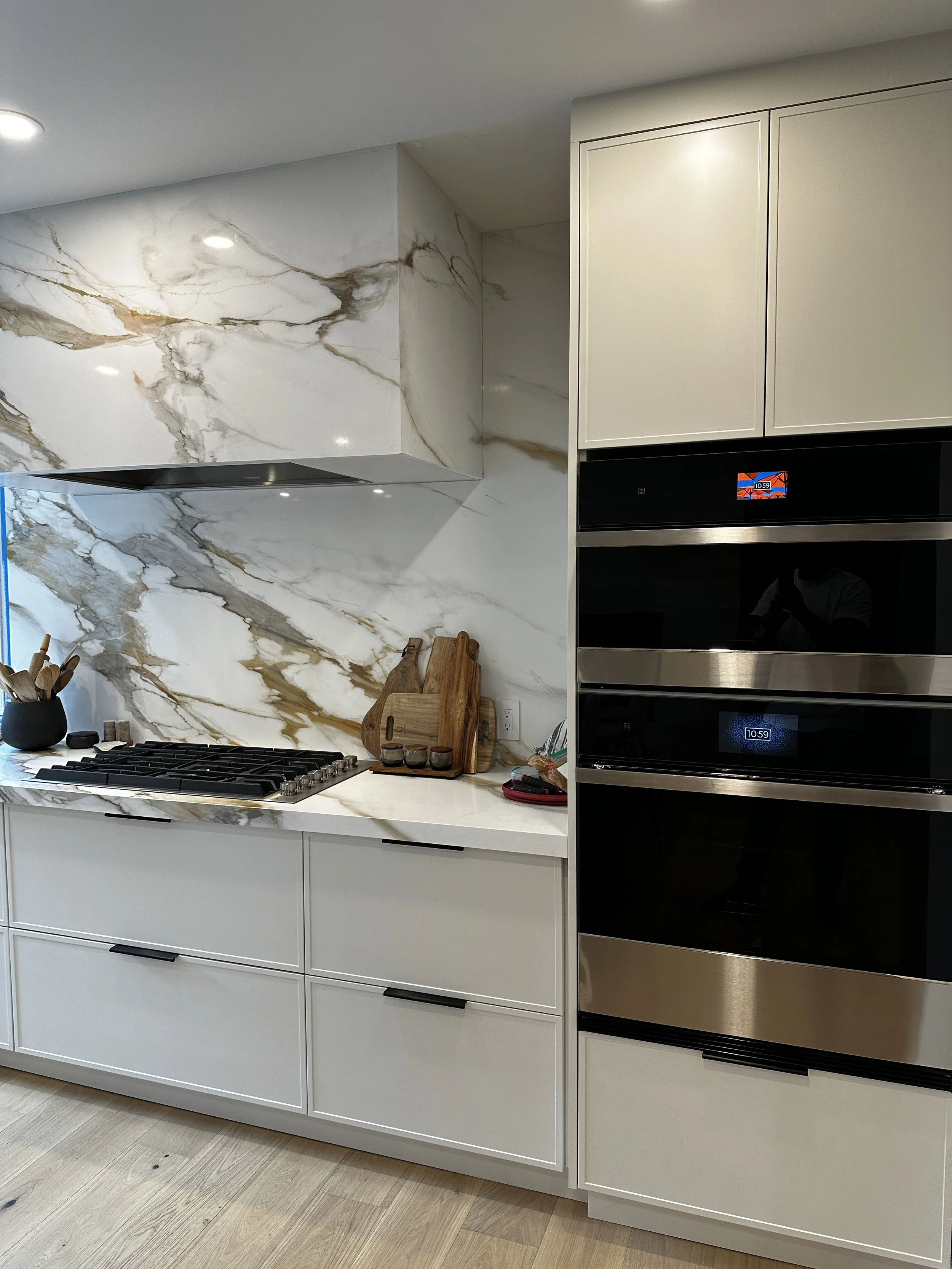 Contemporary kitchen with white cabinetry, marble backsplash, and built-in double oven.