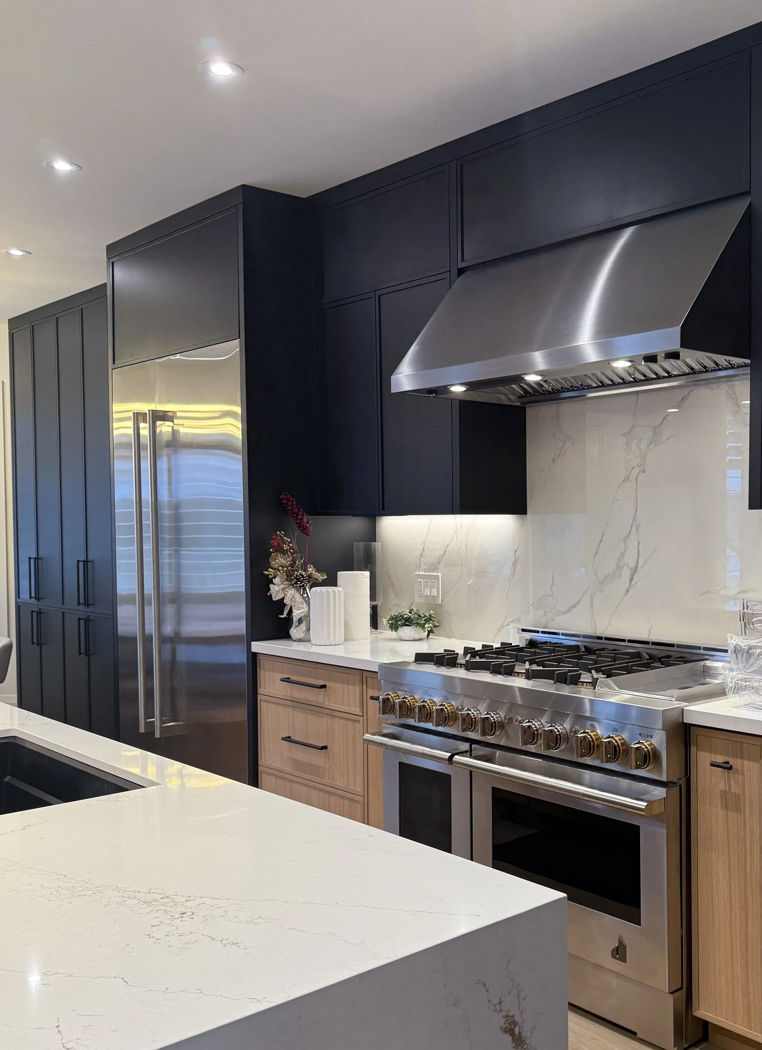 Modern kitchen with black cabinets, stainless steel appliances, white marble backsplash, and a light-colored marble kitchen island.