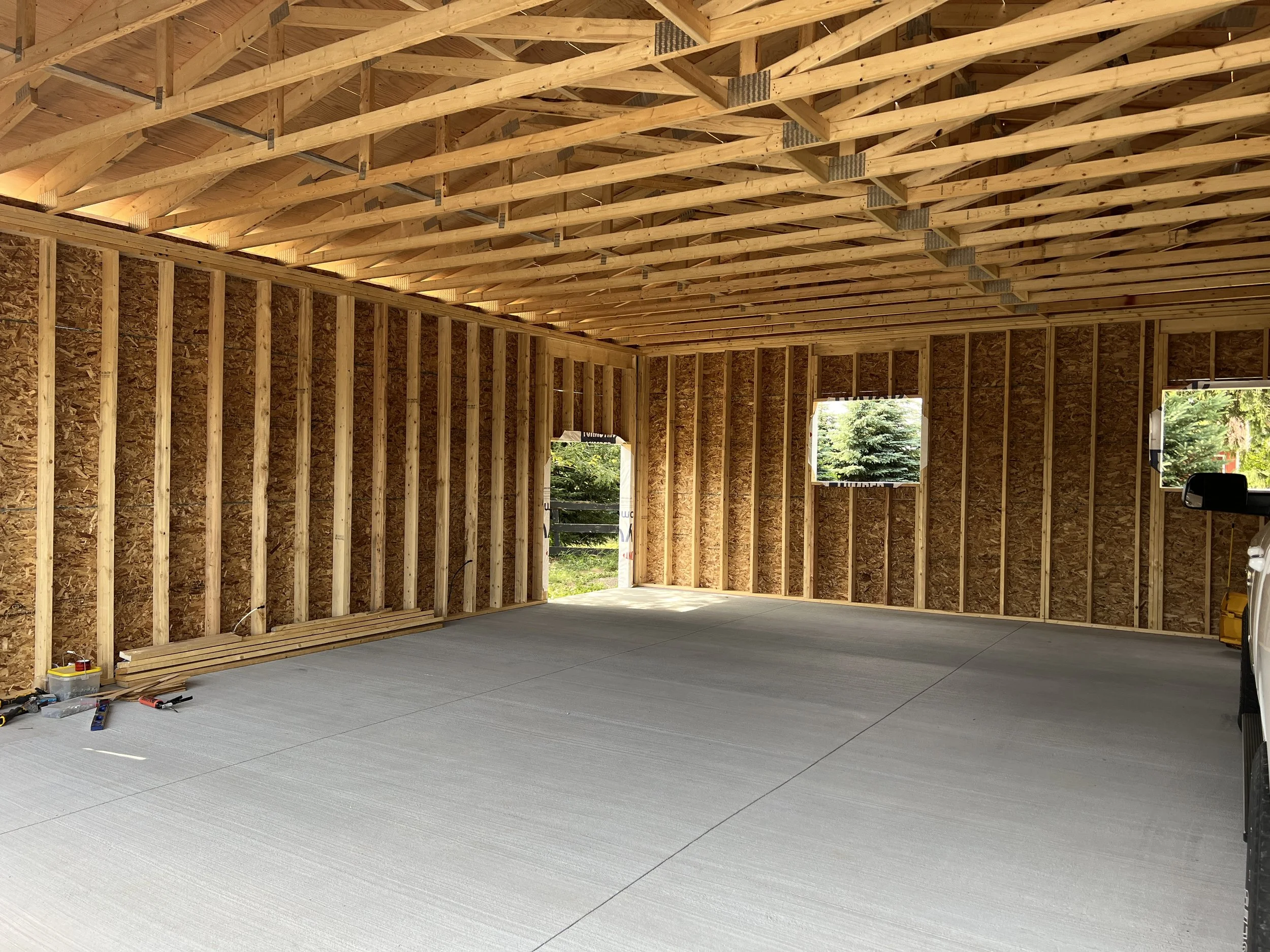 Interior of a building under construction with exposed wooden framing and a concrete floor.