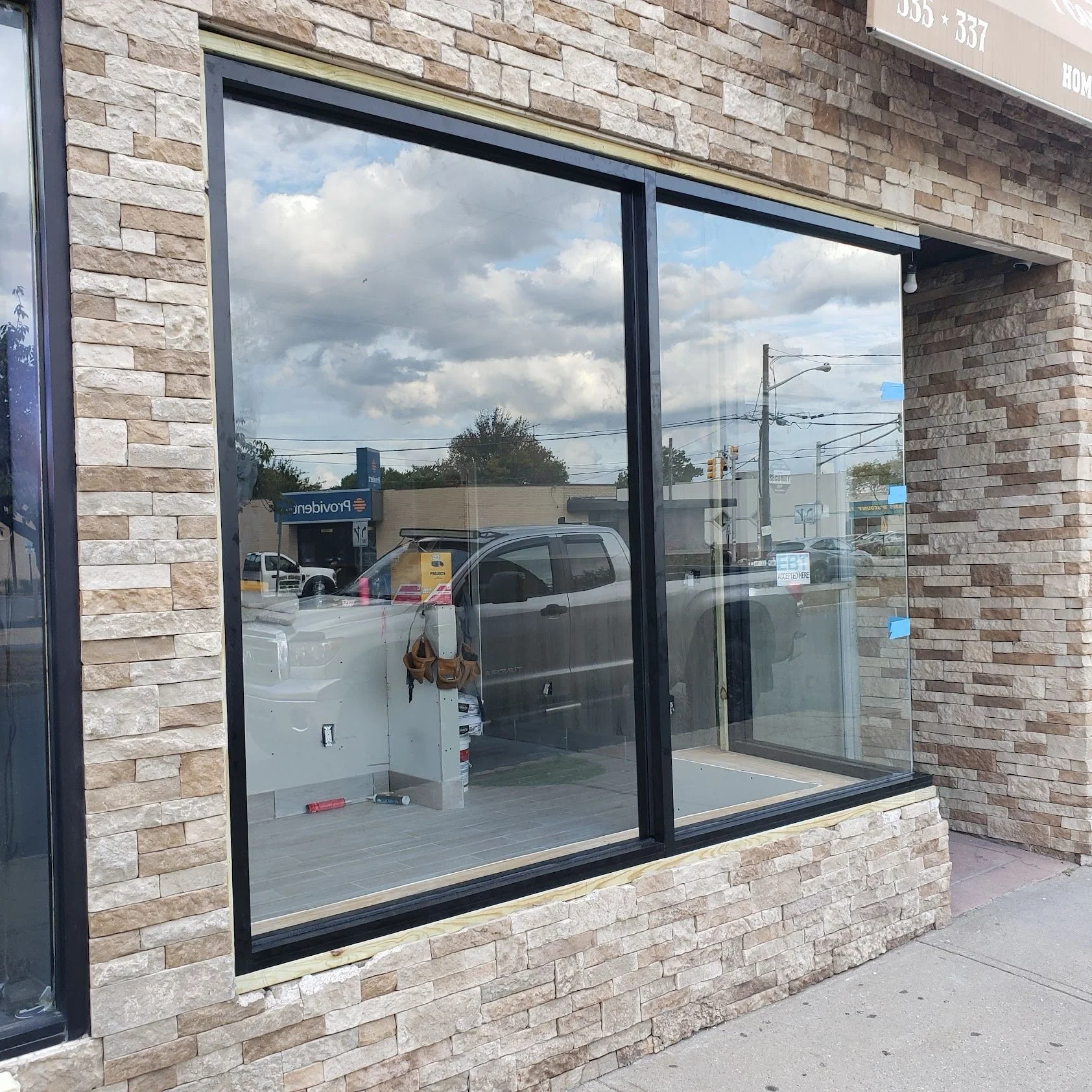 Front view of a store with large glass windows and a beige brick exterior, reflecting the cloudy sky and street scene outside.