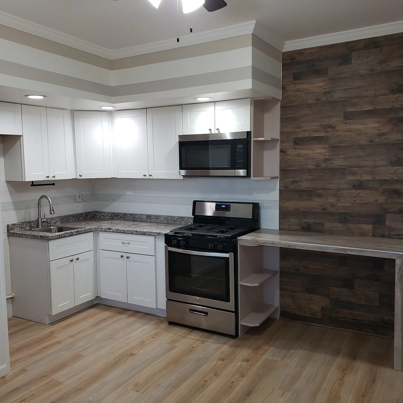 Modern kitchen with white cabinets, a microwave, a stove, and wood-style wall paneling.