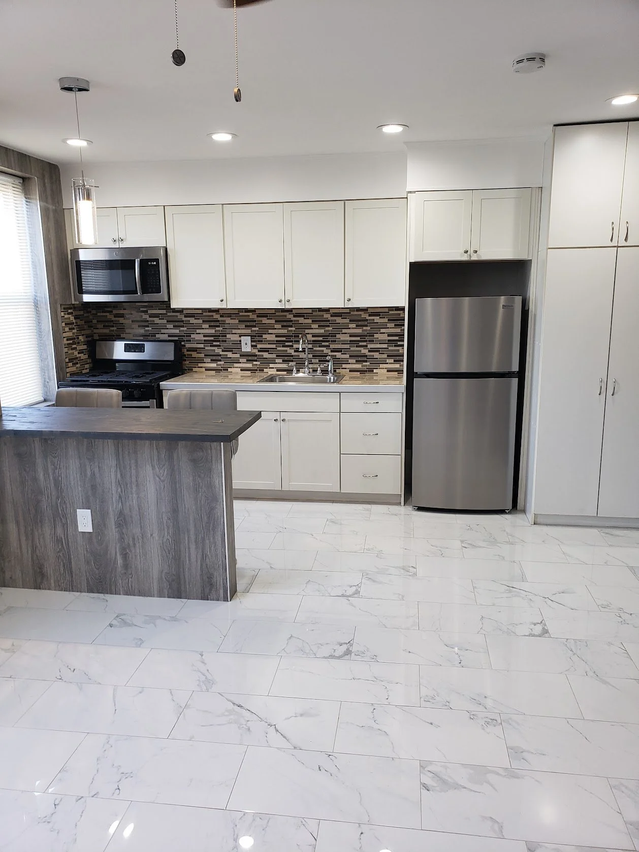 Modern kitchen with white cabinets, stainless steel appliances, a patterned backsplash, and white marble floor tiles.