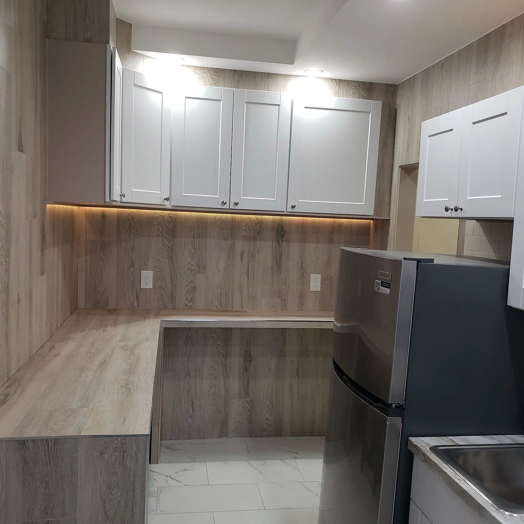 Modern kitchen with white cabinets, wood-paneled walls, and a stainless steel refrigerator.