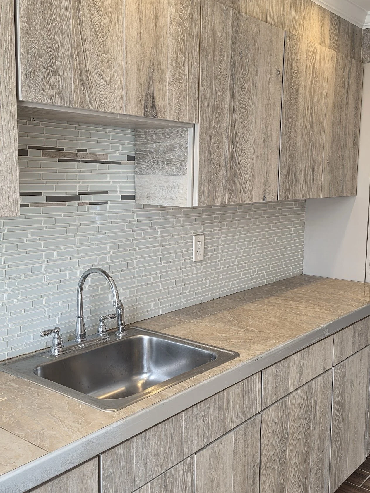 Kitchen with a single sink, wooden cabinets, a tiled backsplash, and a power outlet on the wall.