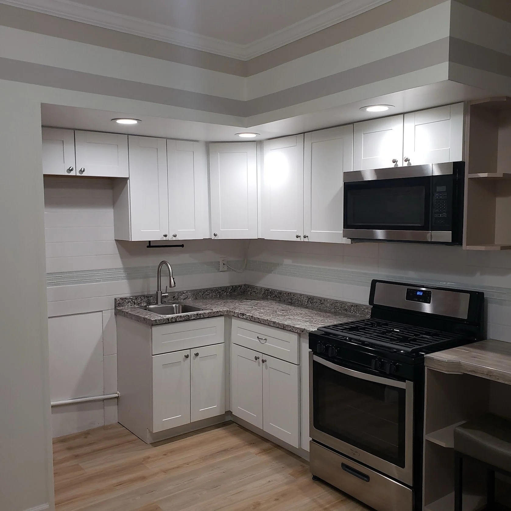 Modern kitchen with white cabinets, granite countertops, stainless steel microwave, and range oven with black stovetop. Recessed ceiling lights and wood flooring.