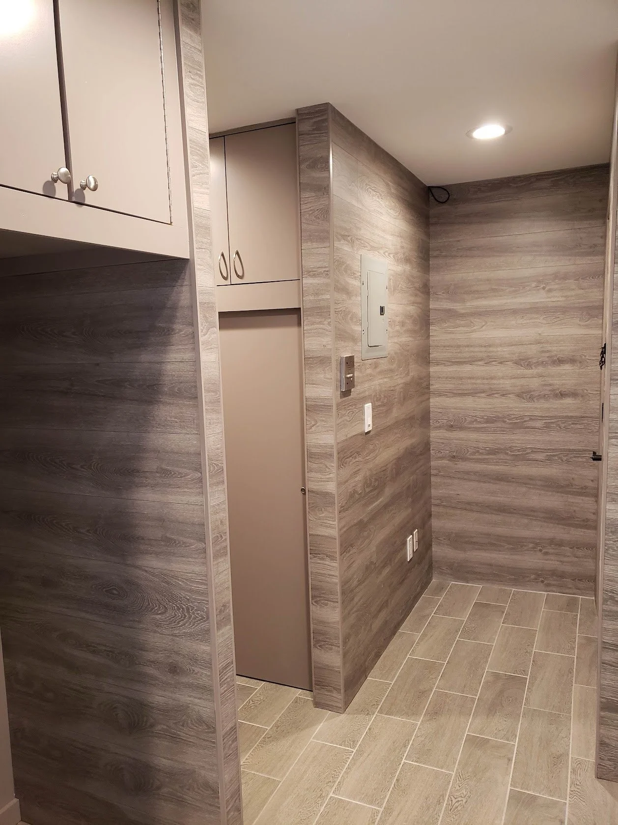 Interior view of a room with wood-paneled walls, a beige door, and tiled flooring. Several electrical panels and outlets are fixed on the wall, with a ceiling light illuminating the space.