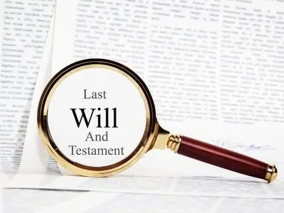 A magnifying glass with a wooden handle focusing on the words 'Last Will And Testament' on a document.