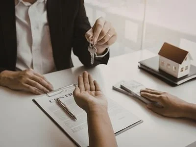 Person handing over a key to another person during a transaction, with documents on the table.