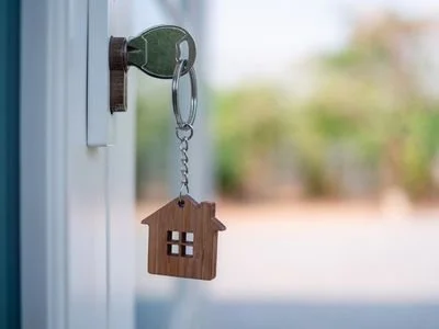 A keychain with a wooden house charm hanging from a door lock.