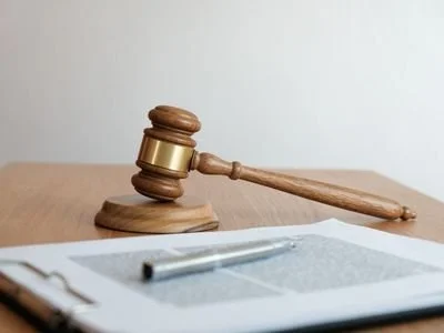 A wooden judge's gavel resting on a sound block on a desk, with a tablet and pen in the foreground.