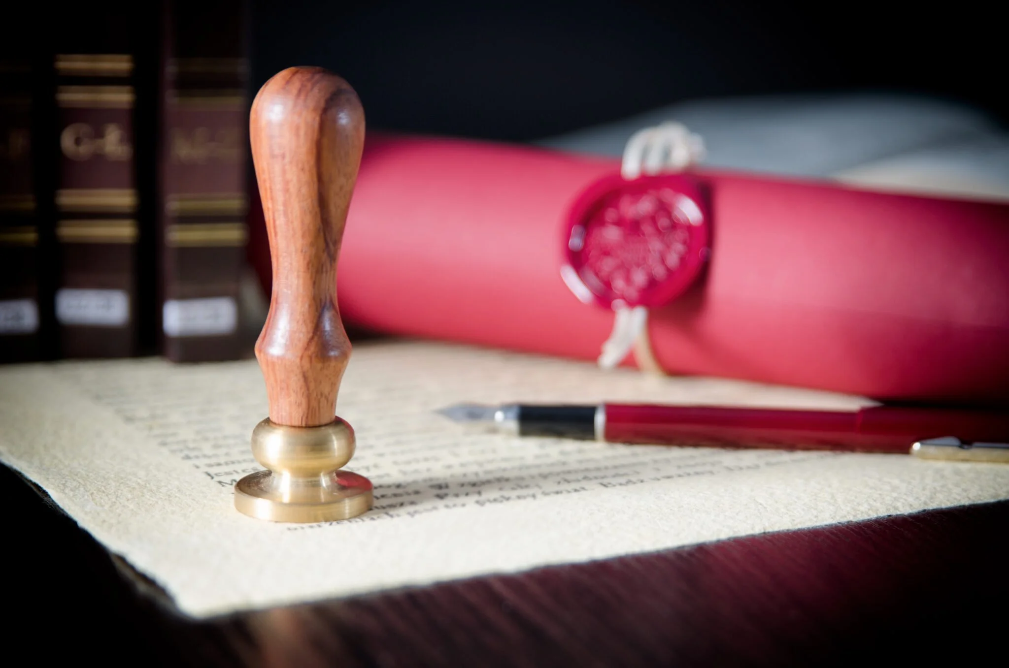 Close-up of a wooden stamp with a brass base on a printed document, with a red diploma roll in the background.