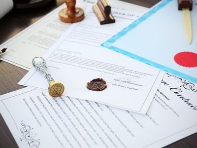 Various legal documents and certificates on a desk, with seals, signatures, a blue folder, and writing instruments.
