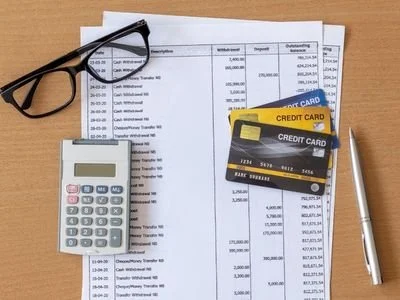Desk with financial documents, eyeglasses, calculator, two credit cards, and a pen.