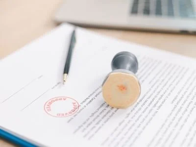 A rubber stamp on an open book or document with text, a black pen, and a laptop keyboard in the background.