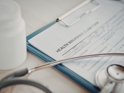 Medical stethoscope, health insurance form, and bottle of pills on a desk.